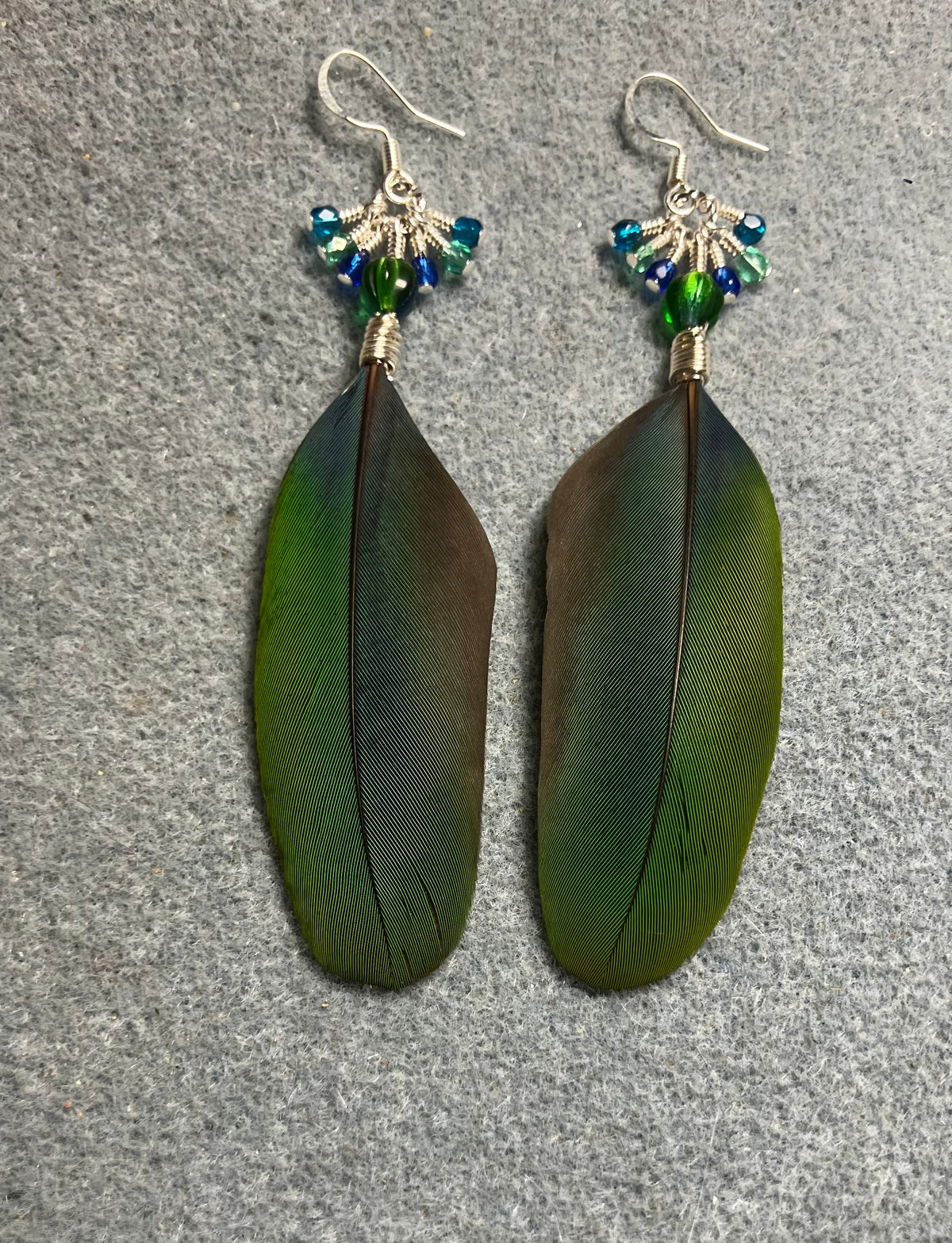 Blue and green blue headed Pionus feather earrings adorned with blue green Czech glass melon beads and small dangling blue, green, and turquoise Czech glass beads.