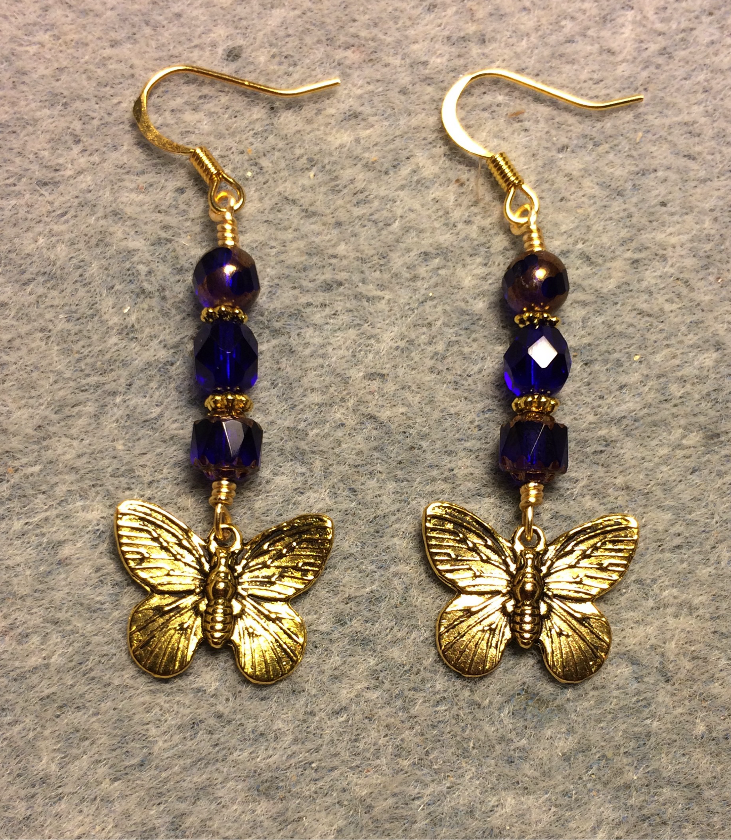 Gold butterfly charm earrings adorned with cobalt blue Czech glass beads.