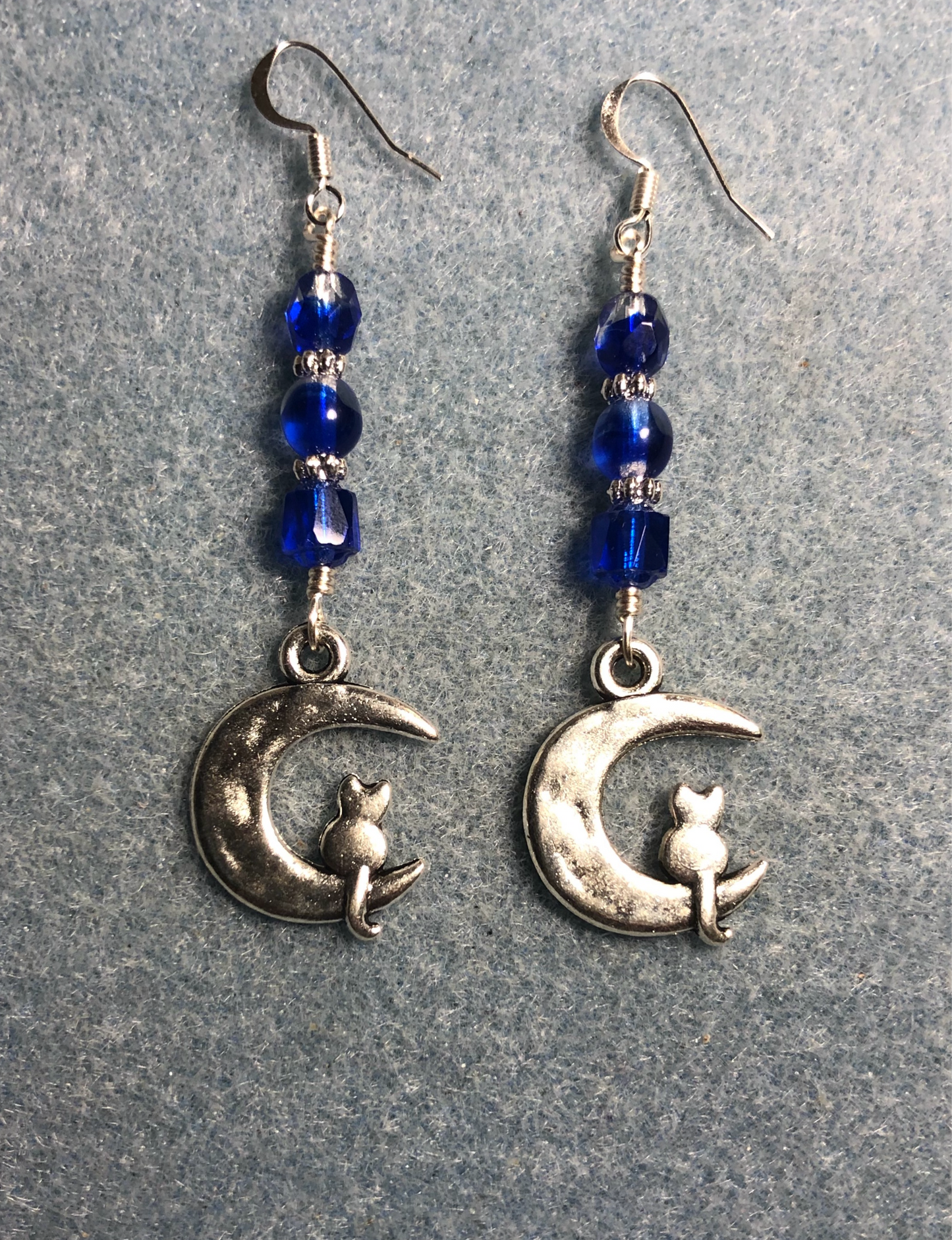 Silver cat sitting on a quarter moon charm earrings adorned with dark blue Czech glass beads