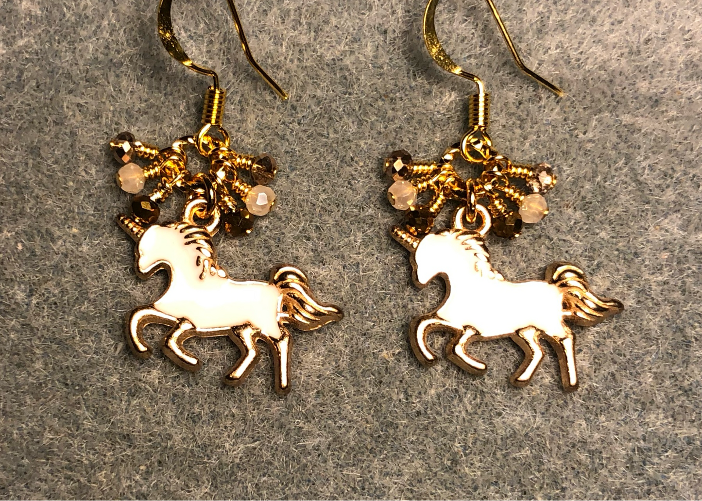 Small white and gold enamel unicorn charm earrings adorned with tiny dangling white and gold Chinese crystal beads.