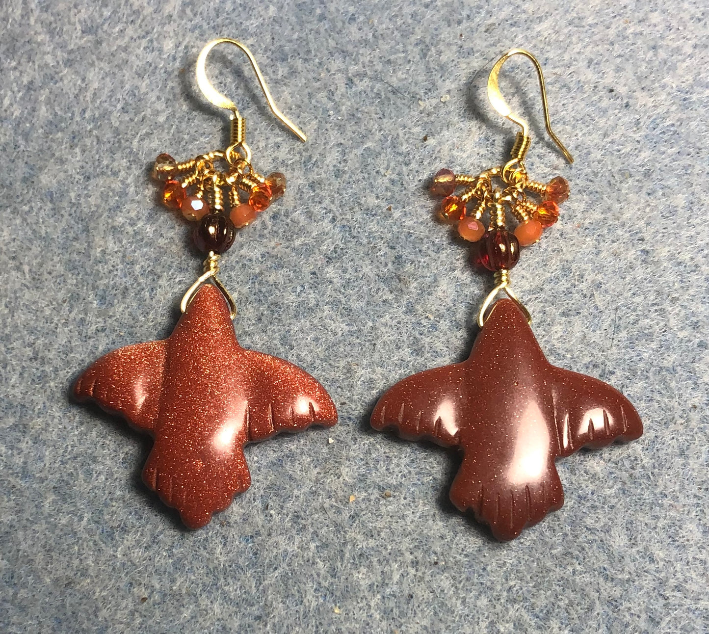 Large orange goldstone gemstone flying eagle bead earrings adorned with tiny dangling orange Chinese crystal beads.
