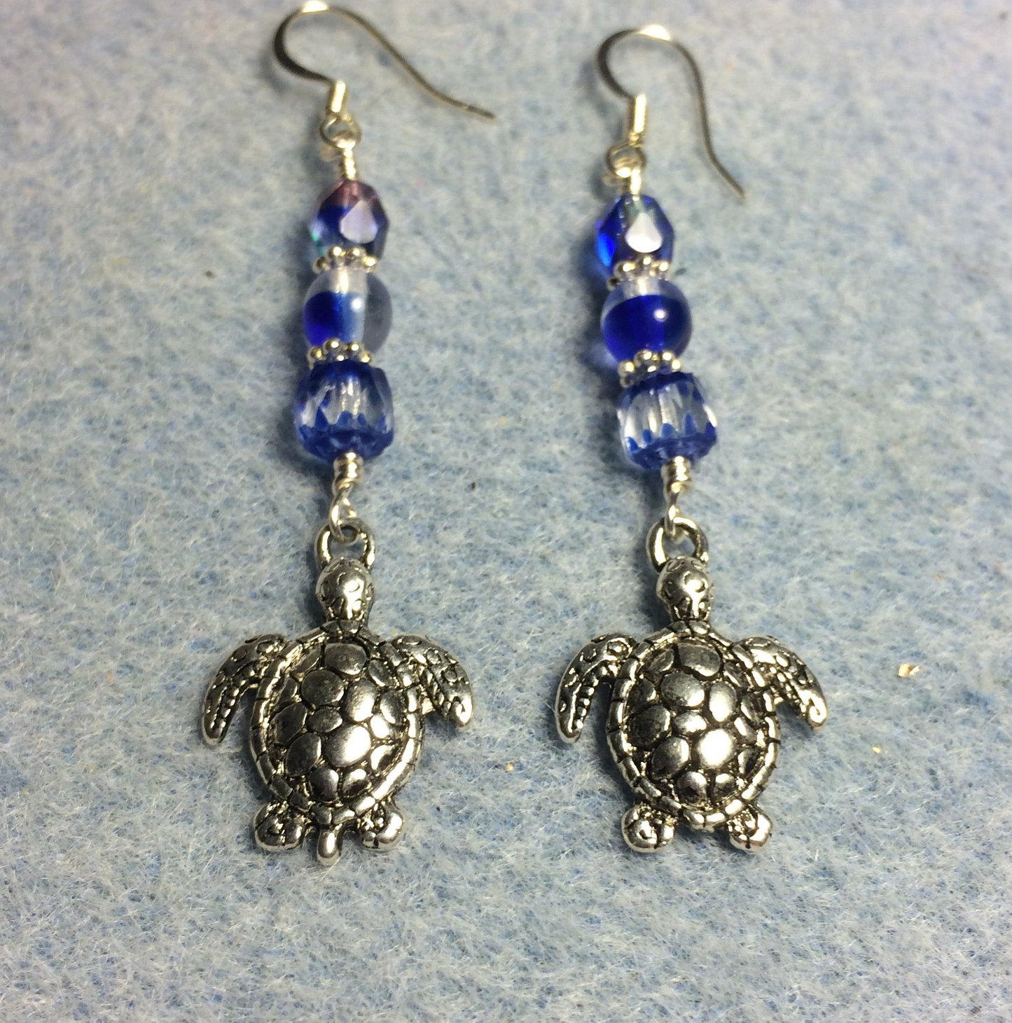 Silver sea turtle charm earrings adorned with dark blue and clear Czech glass beads.