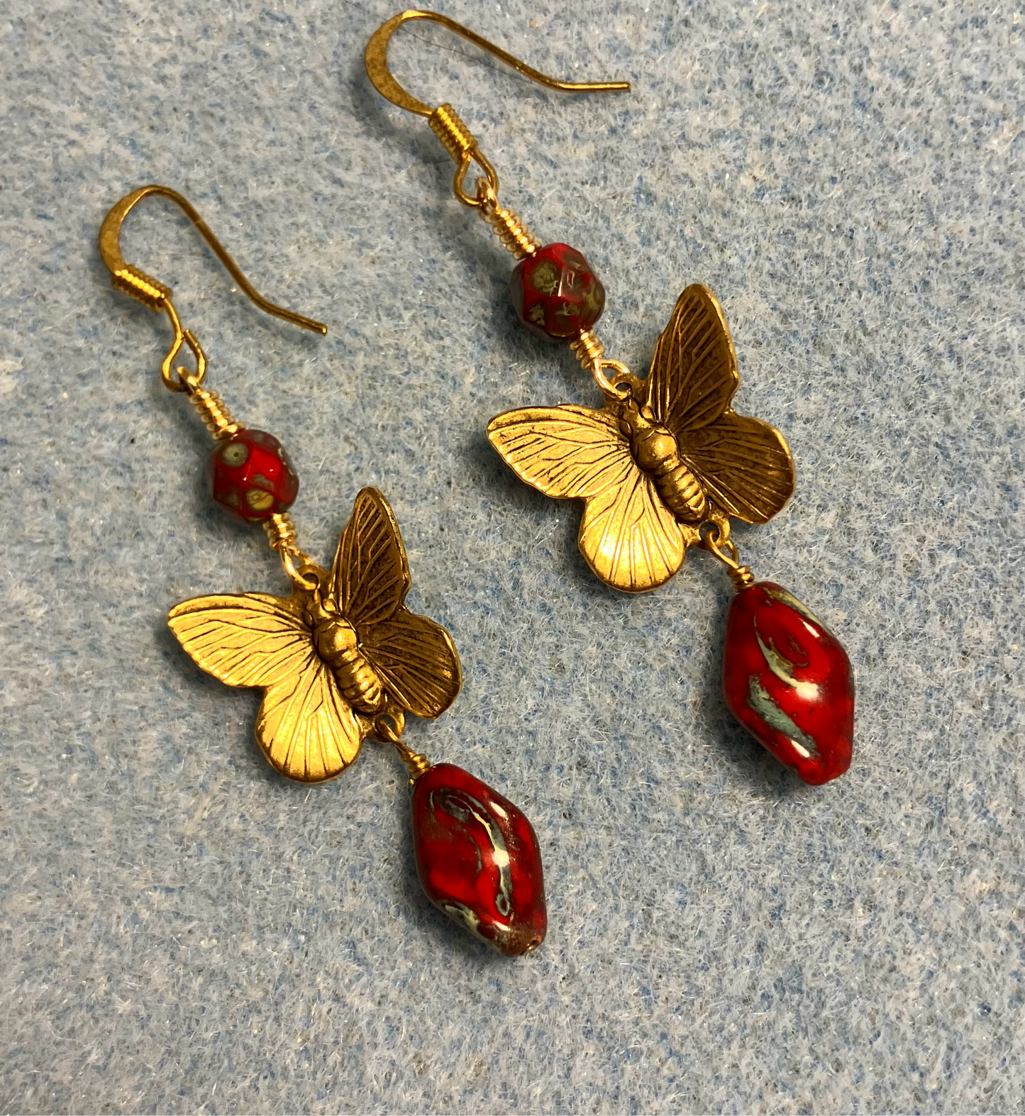 Gold butterfly charm connector earrings adorned with red Picasso Czech glass twist beads and red Picasso Czech glass beads.