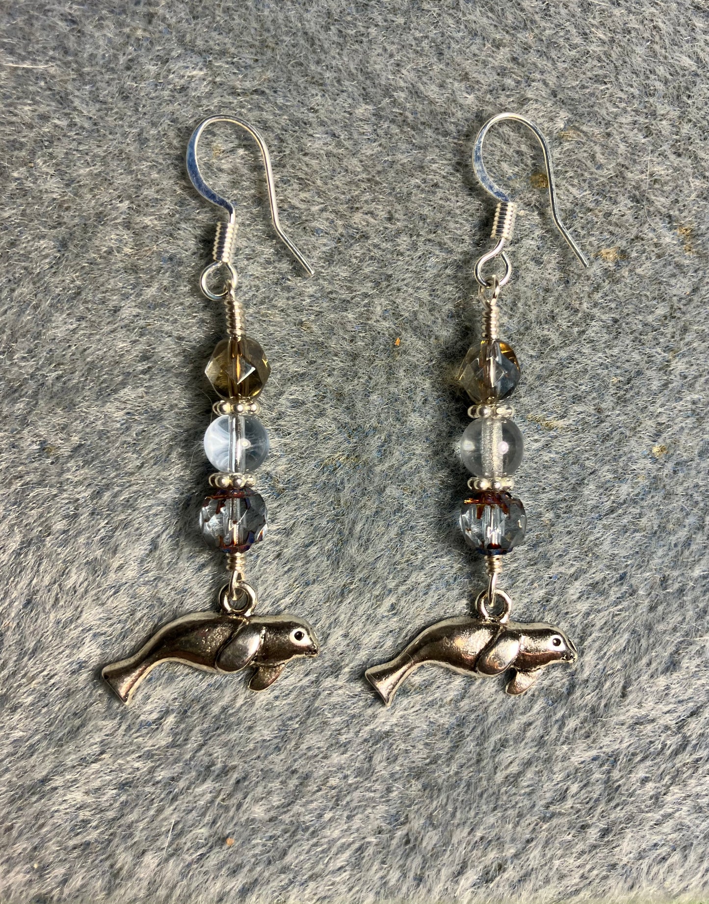 Silver manatee charm earrings adorned with light blue Czech glass beads.