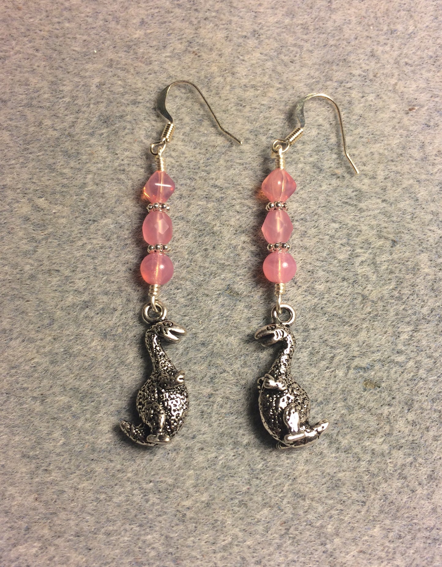Silver dinosaur charm earrings adorned with milky pink Czech glass beads.