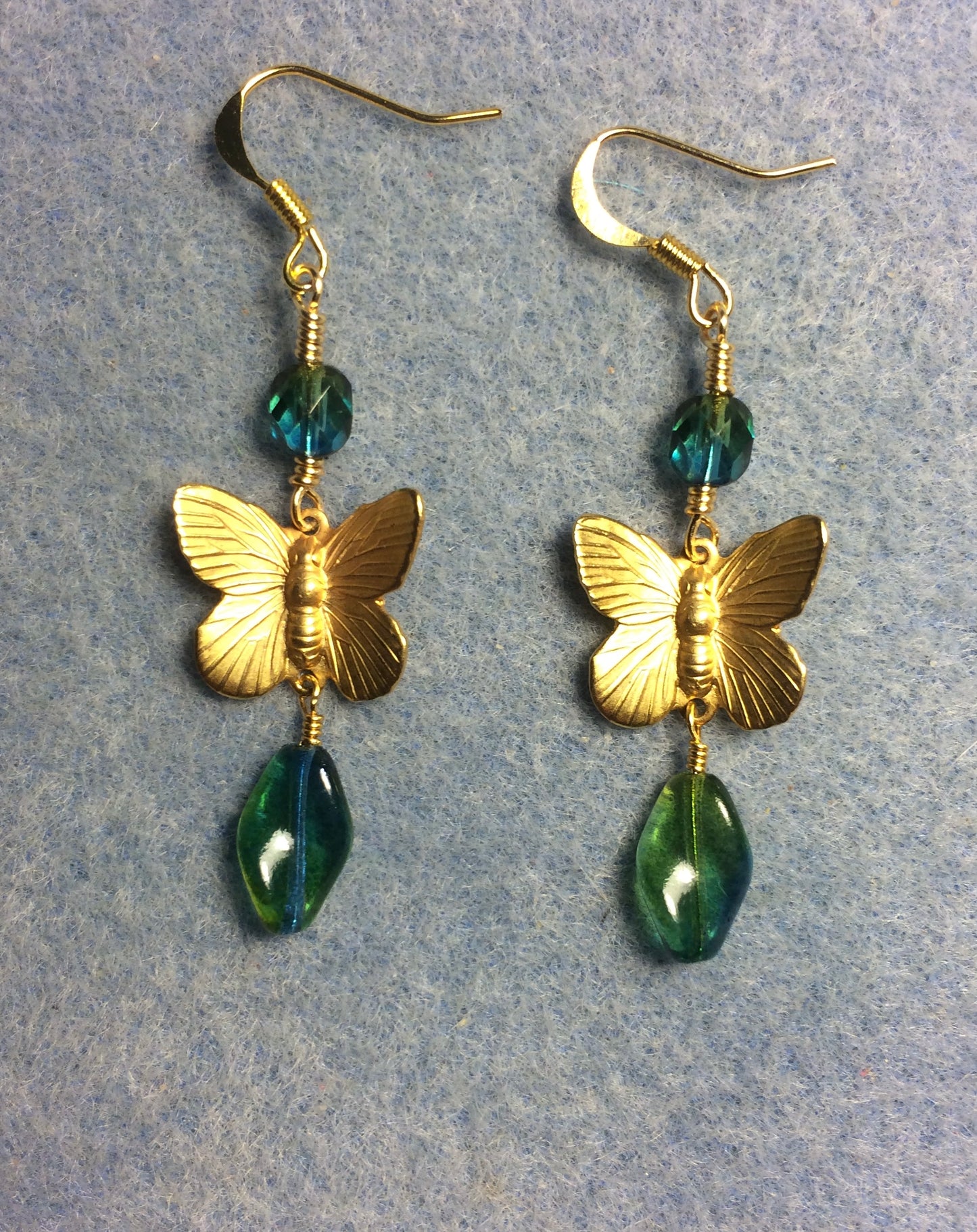 Gold butterfly charm connector earrings adorned with blue green Czech glass twist beads and blue green Czech glass beads.
