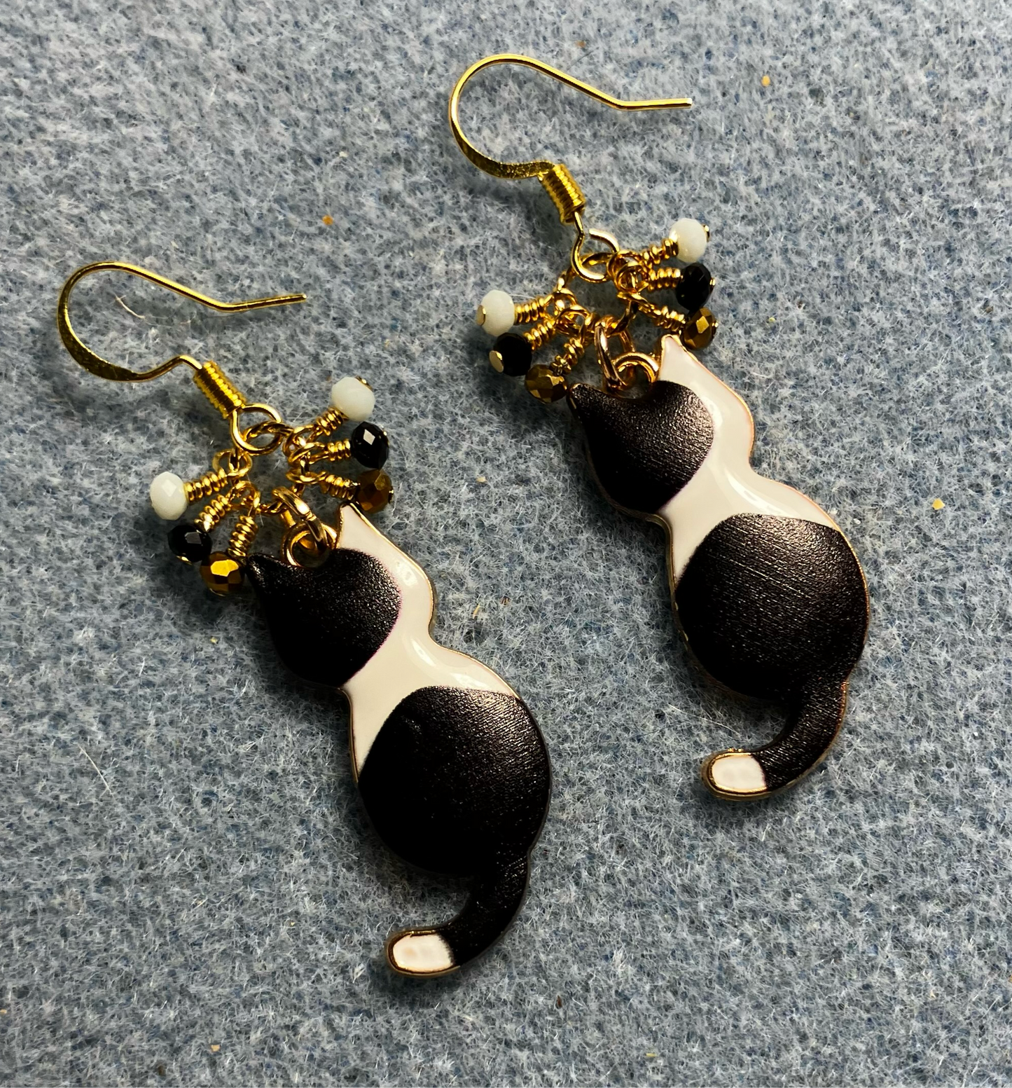 Black and white enamel cat charm earrings adorned with tiny dangling gold, black, and white Chinese crystal beads.