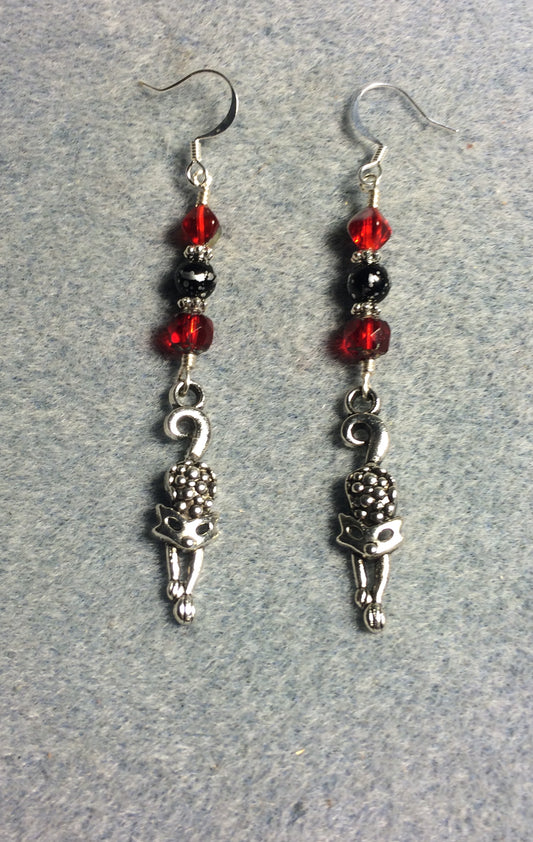 Silver stretching cat charm earrings adorned with red and black Czech glass melon beads.