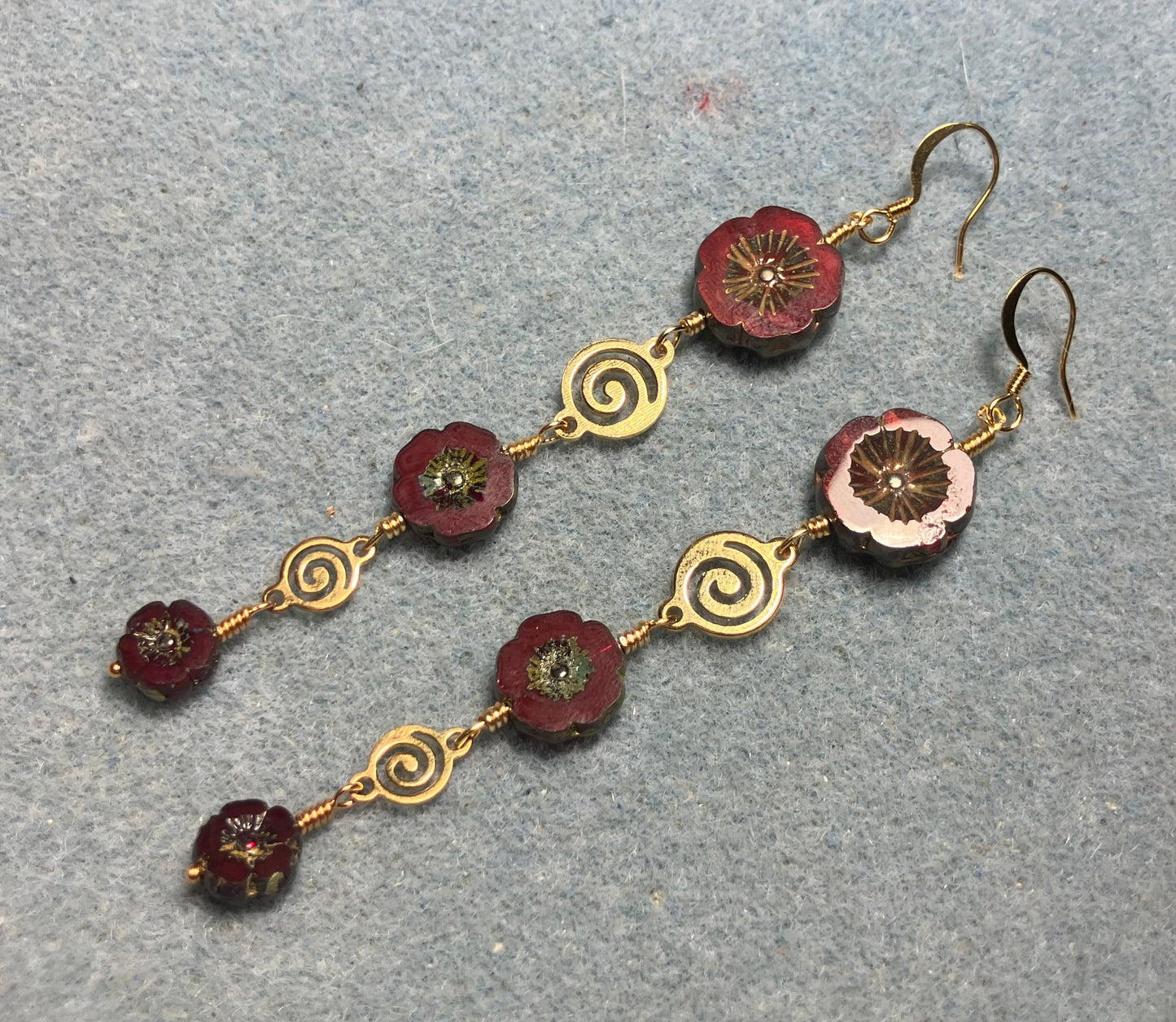 Extra long dark red flower bead earrings made with three sizes of dark red Czech glass pansy beads joined by gold swirly connectors.