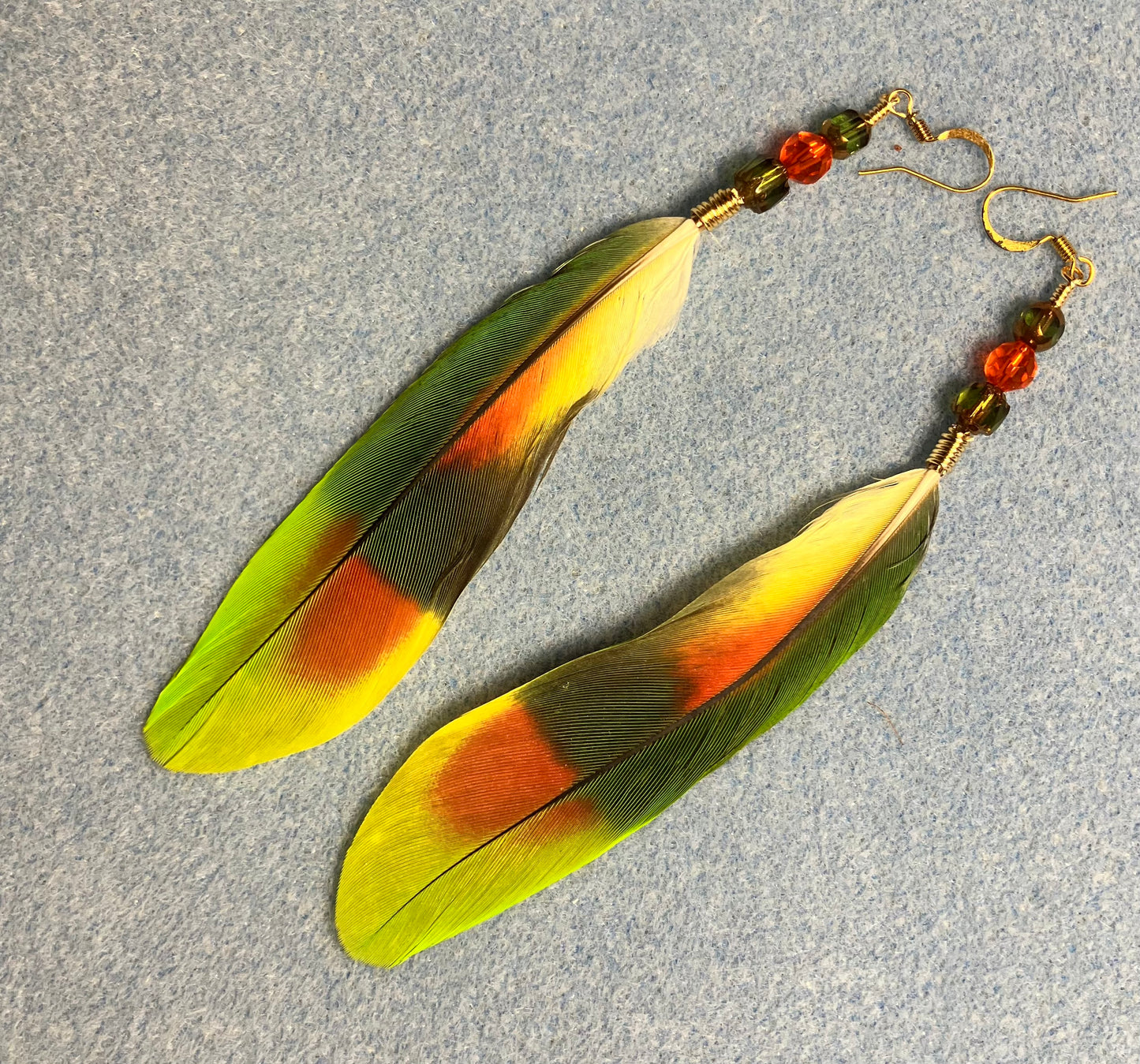 Orange winged Amazon parrot feather earrings adorned with green and orange Czech glass beads.