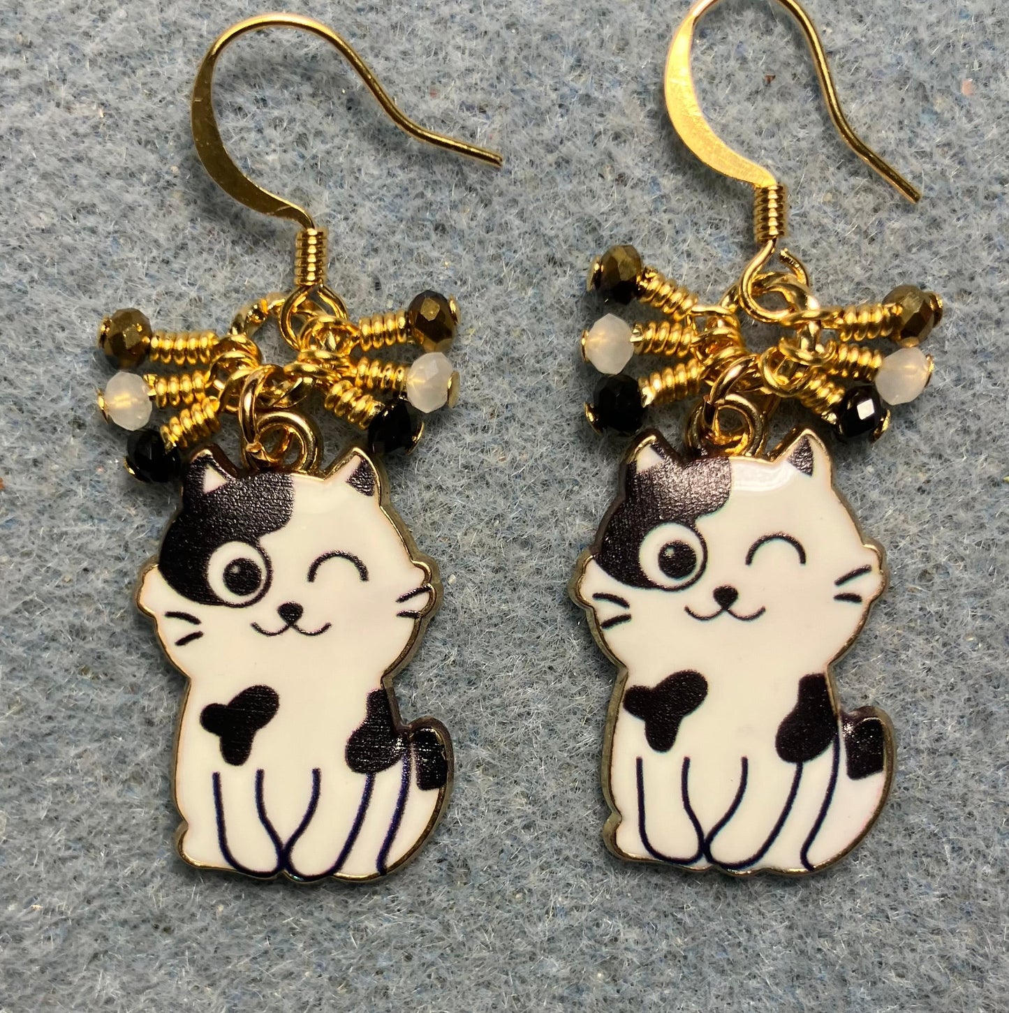 Black and white enamel cat charm earrings adorned with tiny dangling black, white, and gold Chinese crystal beads.