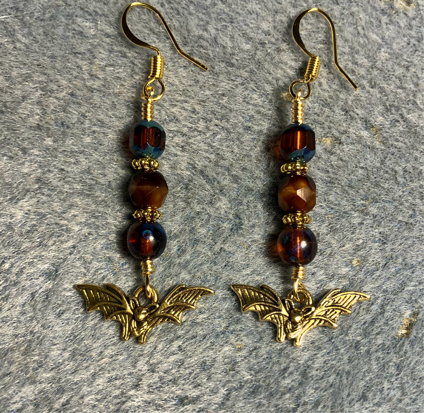 Small gold bat charm earrings adorned with blue Czech glass beads