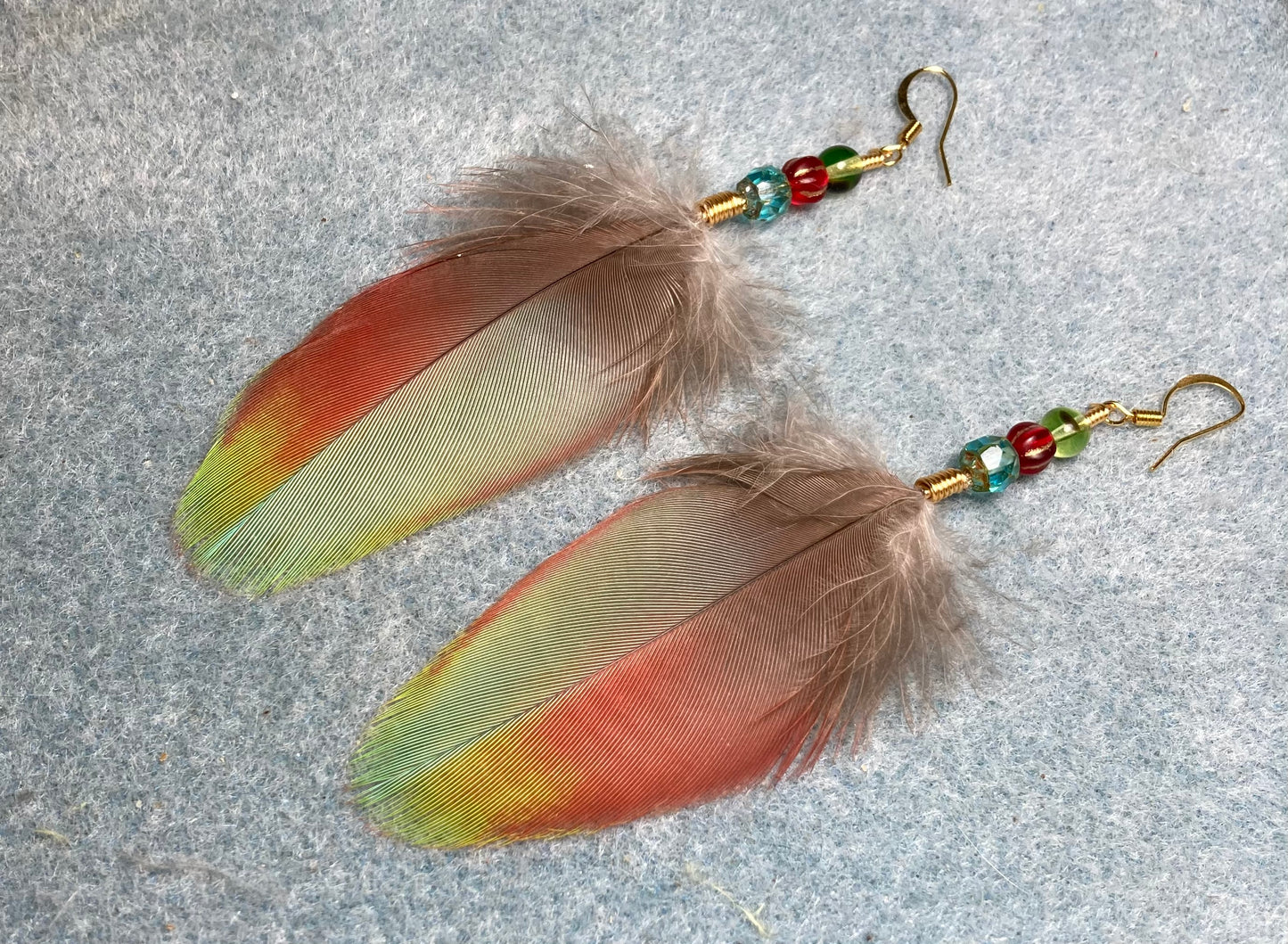 Red and turquoise greenwinged macaw feather earrings adorned with red, turquoise, and green Czech glass beads.