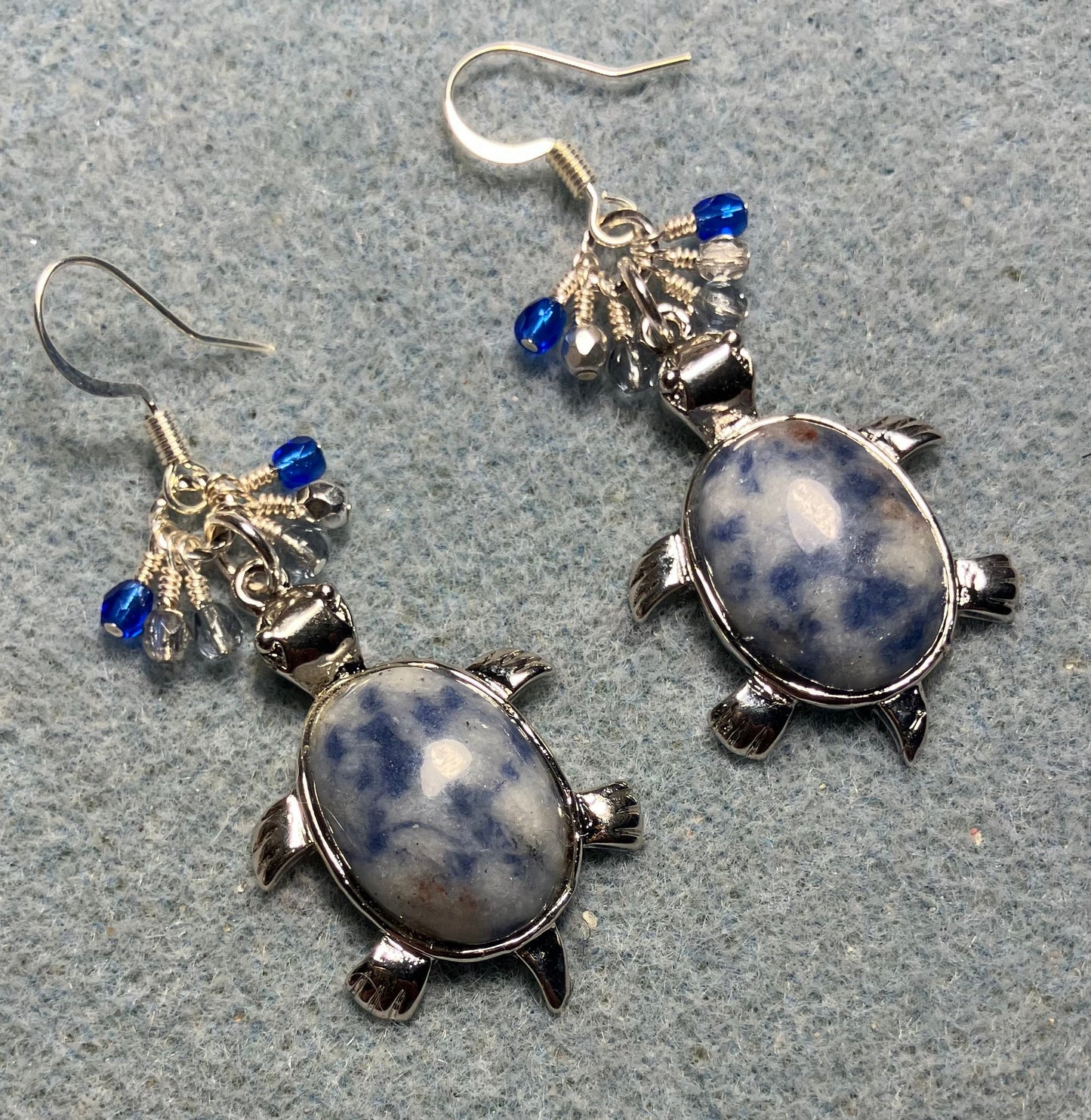 Large silver and blue sodalite gemstone turtle charm earrings adorned with small dangling dark blue, light blue, and silver Czech glass beads.