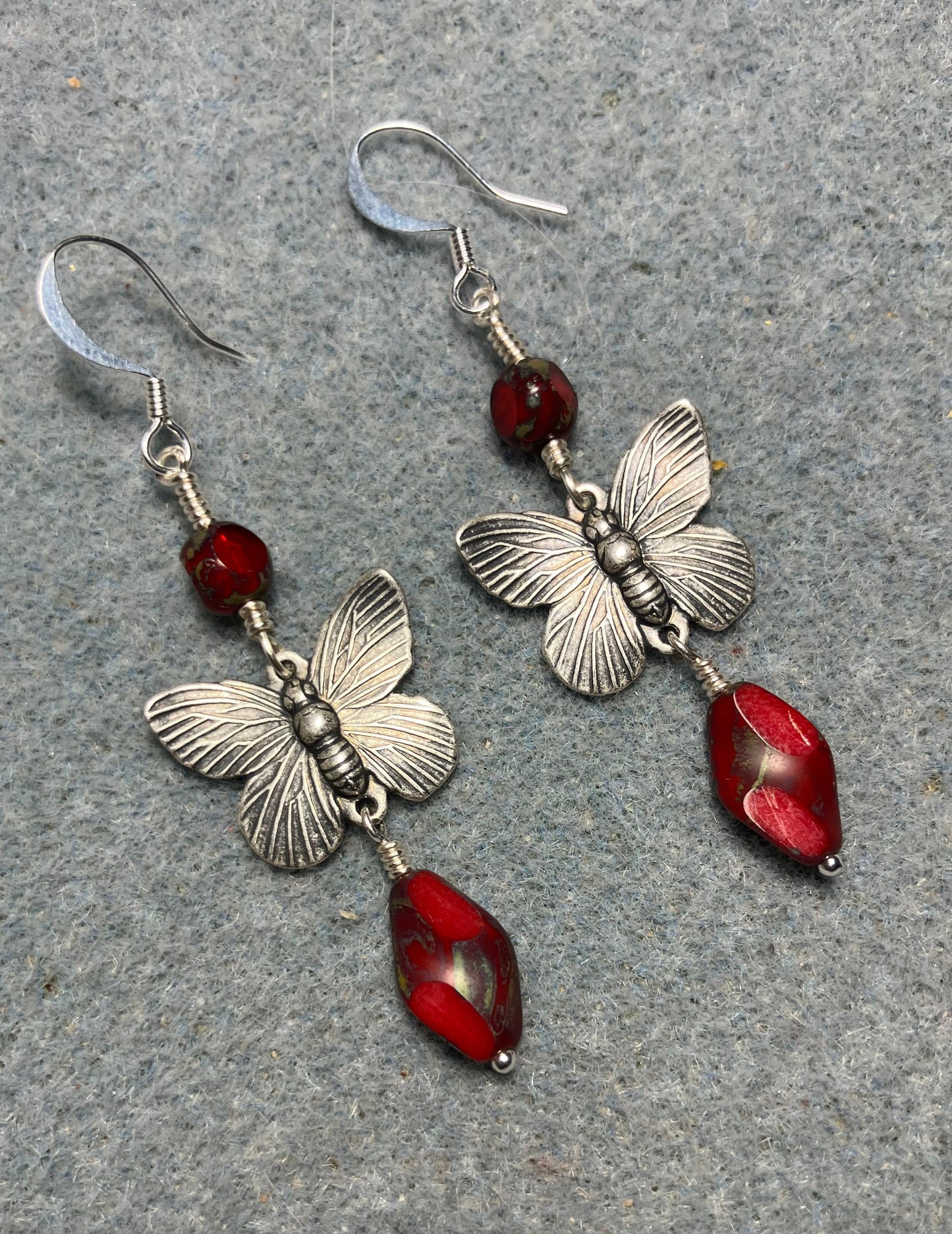 Silver butterfly connector charm earrings adorned with opaque red Czech glass twist beads and opaque red Czech glass beads.