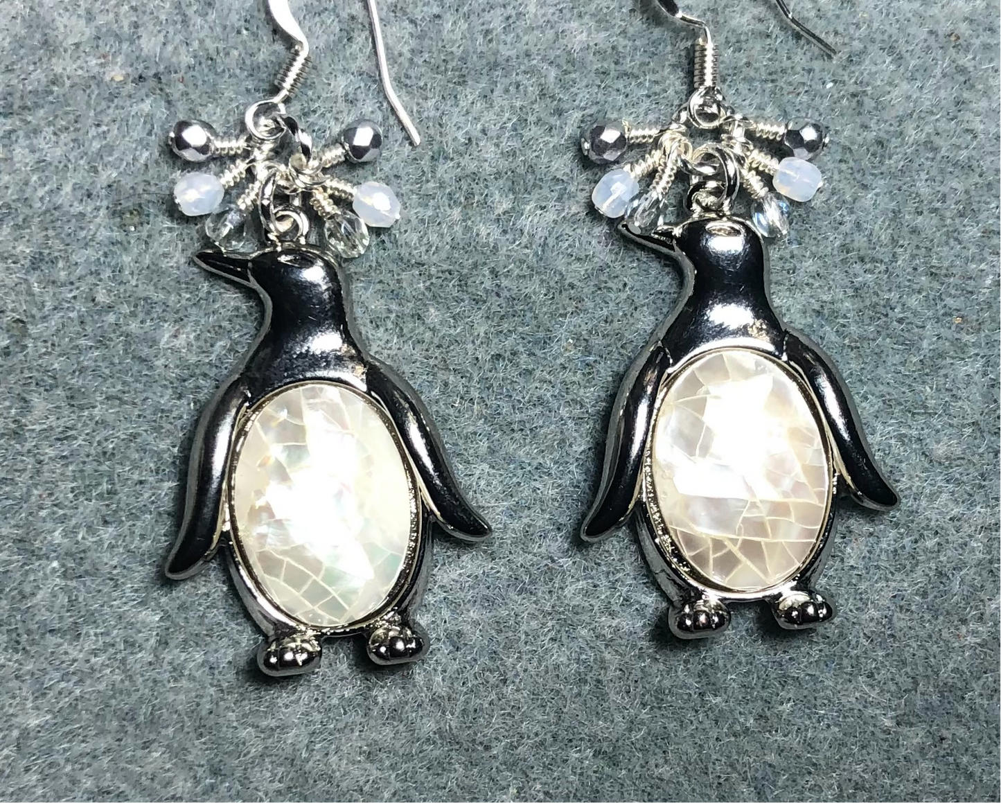 Large silver and mother of pearl penguin charm earrings adorned with small dangling white, silver, and clear Czech glass beads.