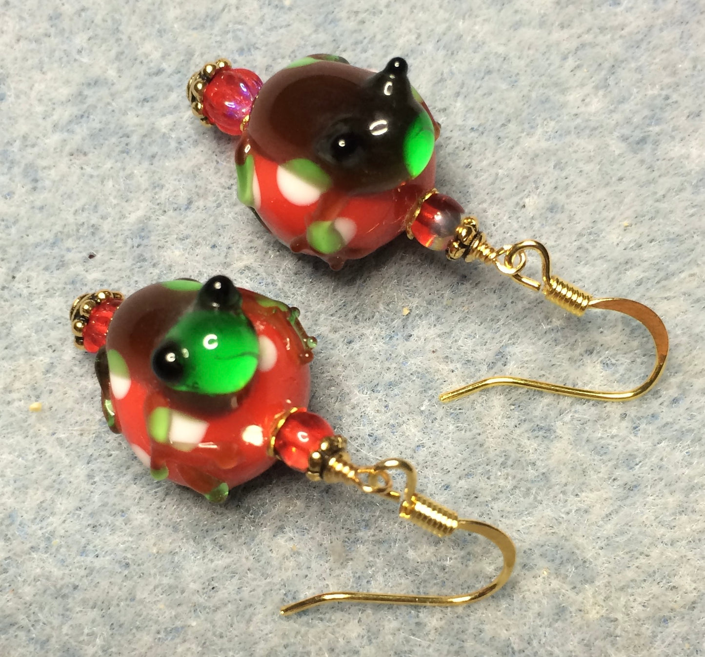 Red, green, and brown lamp work frog bead earrings adorned with red Czech glass beads.