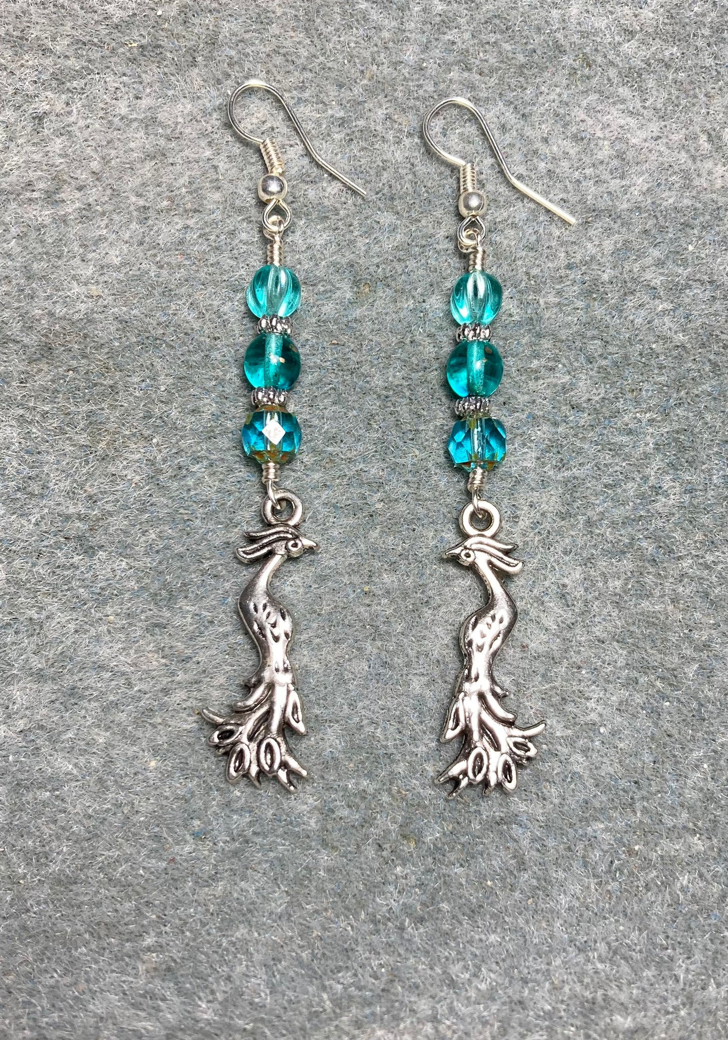 Long silver Phoenix charm earrings adorned with turquoise Czech glass beads.