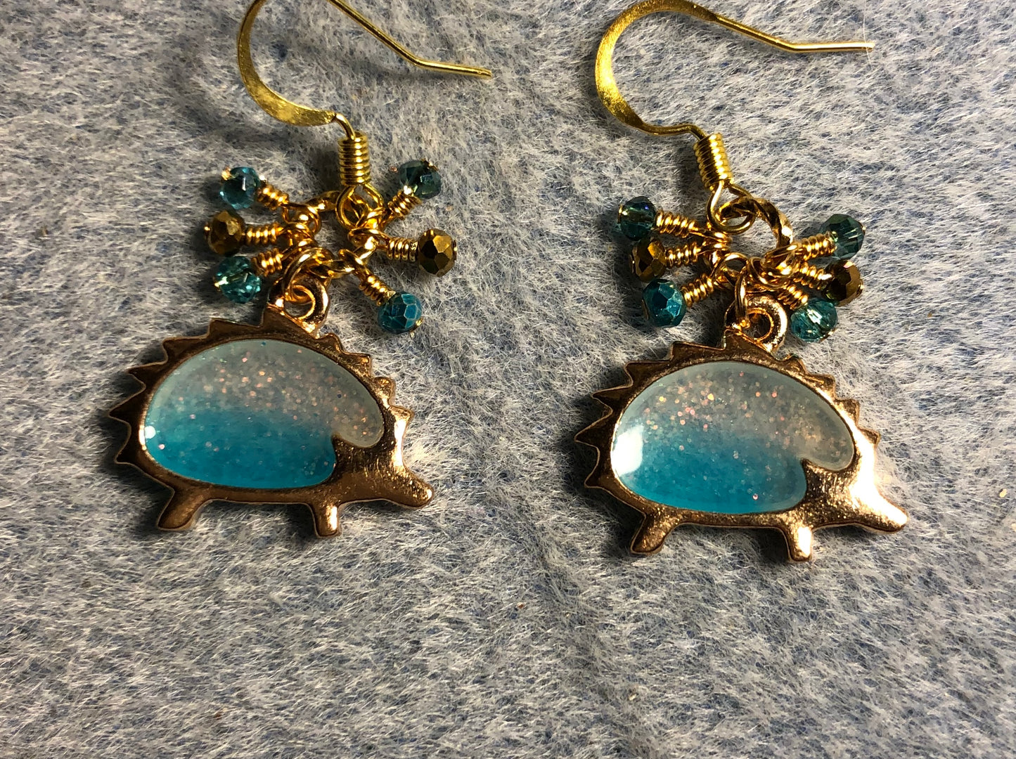Gold and sparkly turquoise resin hedgehog charm earrings adorned with tiny dangling turquoise, gold, and teal Chinese crystal beads.