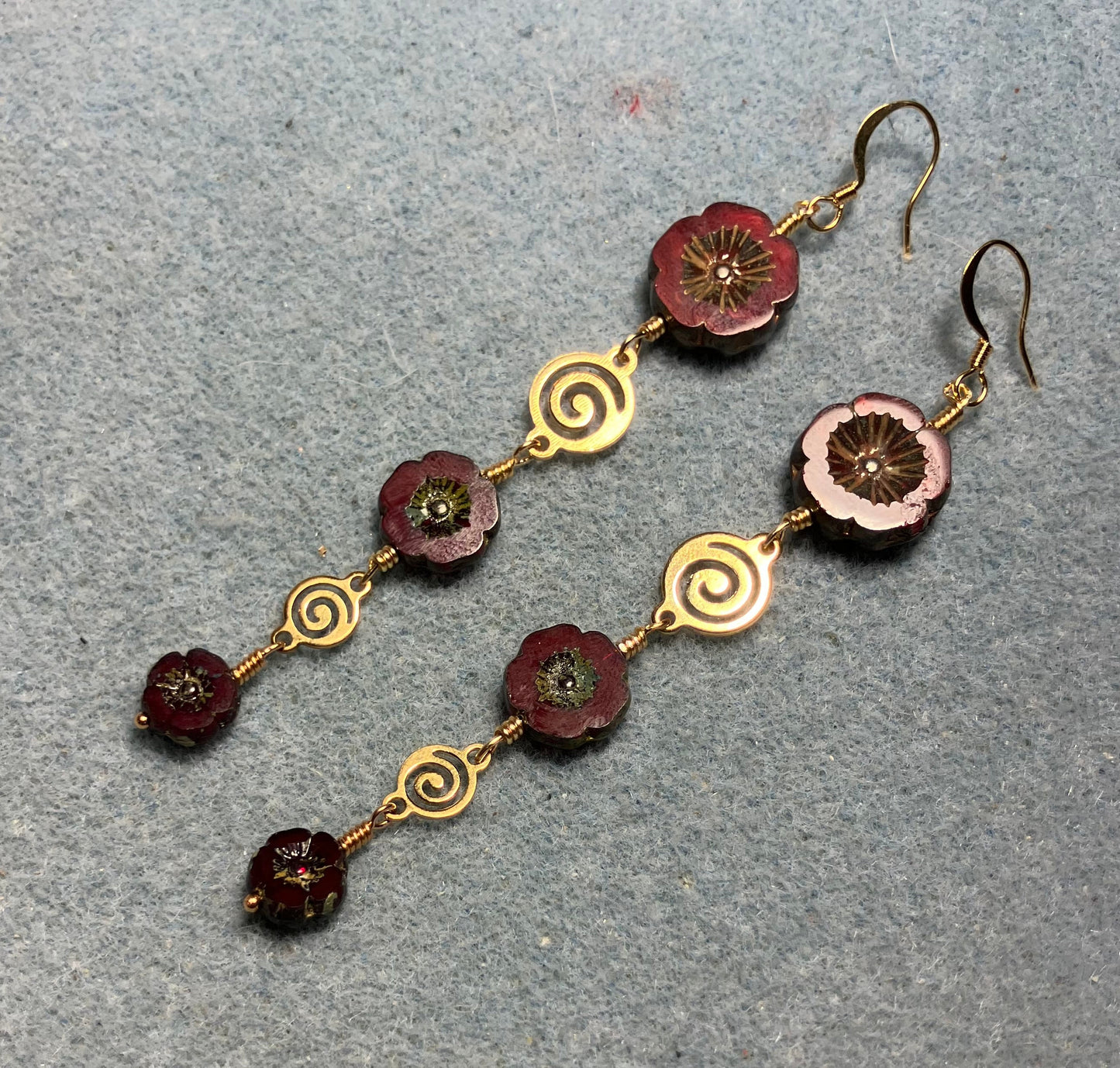 Extra long dark red flower bead earrings made with three sizes of dark red Czech glass pansy beads joined by gold swirly connectors.