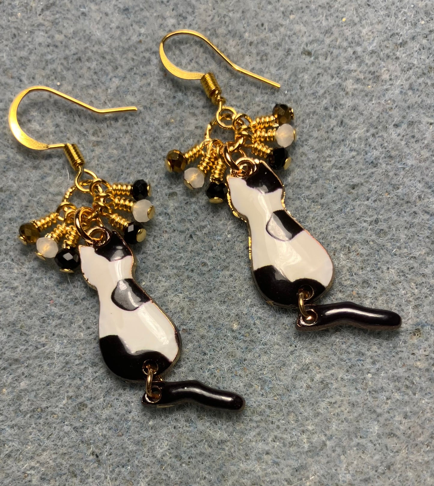 Black, white, and gold enamel cat charm earrings adorned with tiny dangling black, white, and gold Chinese crystal beads.