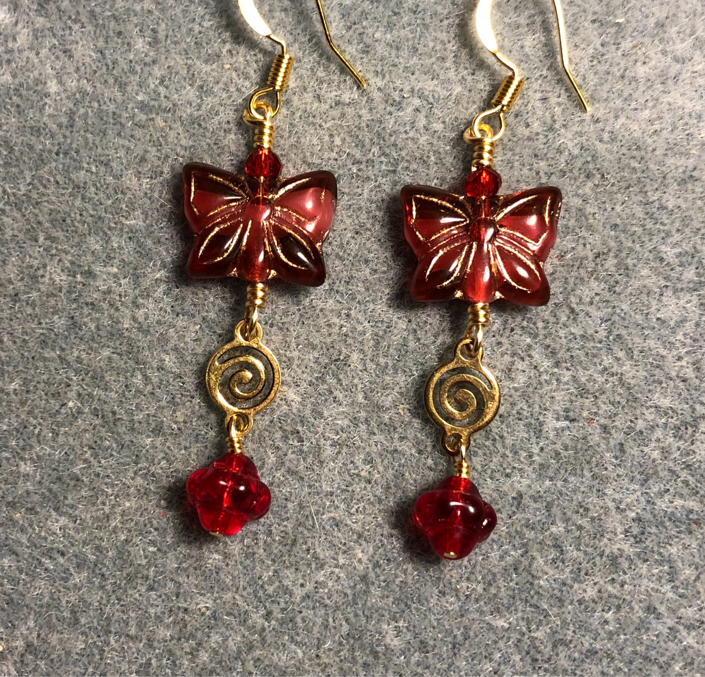 Cranberry red Czech glass butterfly bead earrings adorned with gold swirly connectors and cranberry red Czech glass Saturn beads.