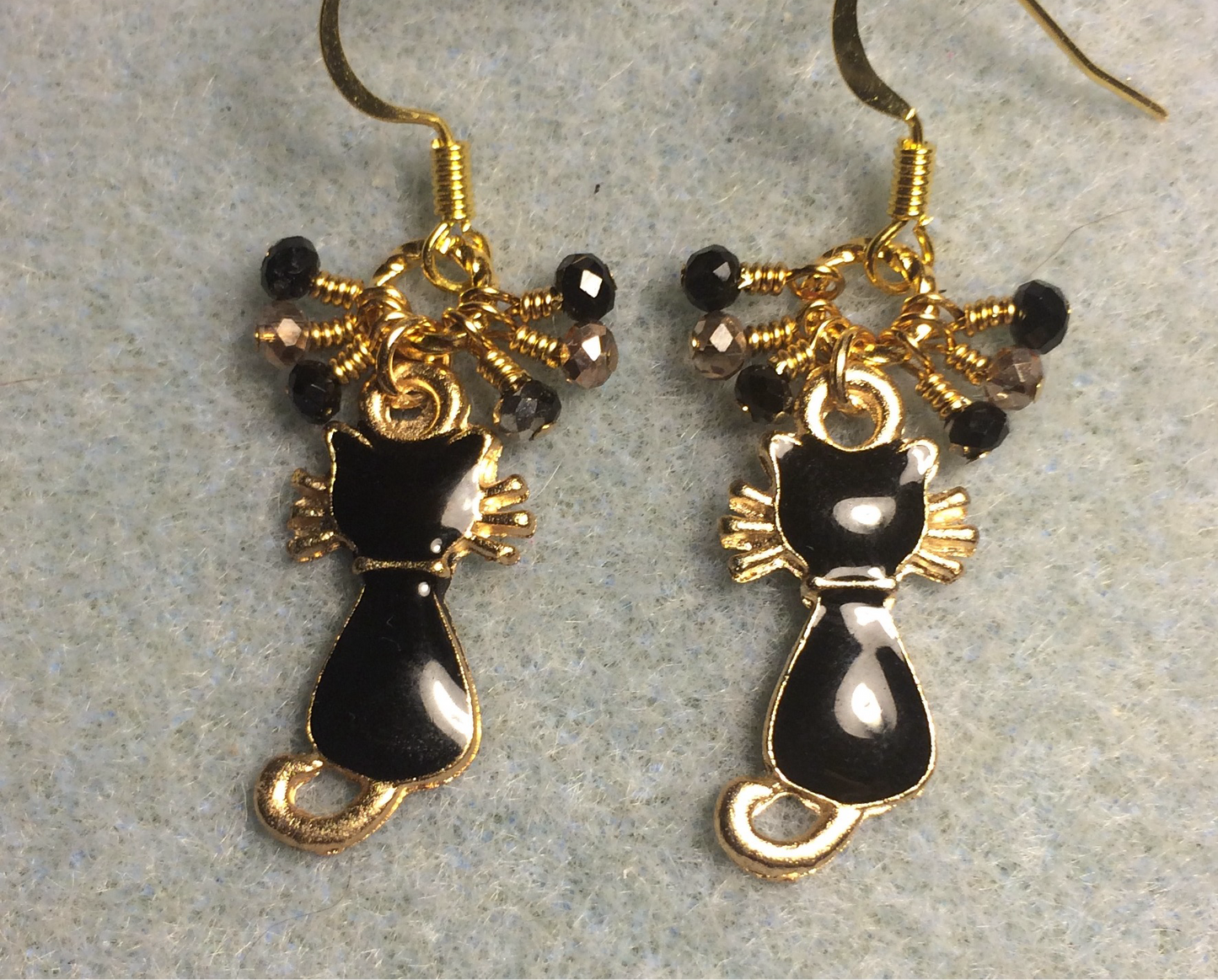 Small black and gold enamel cat charm earrings adorned with tiny dangling black and gold Chinese crystal beads.