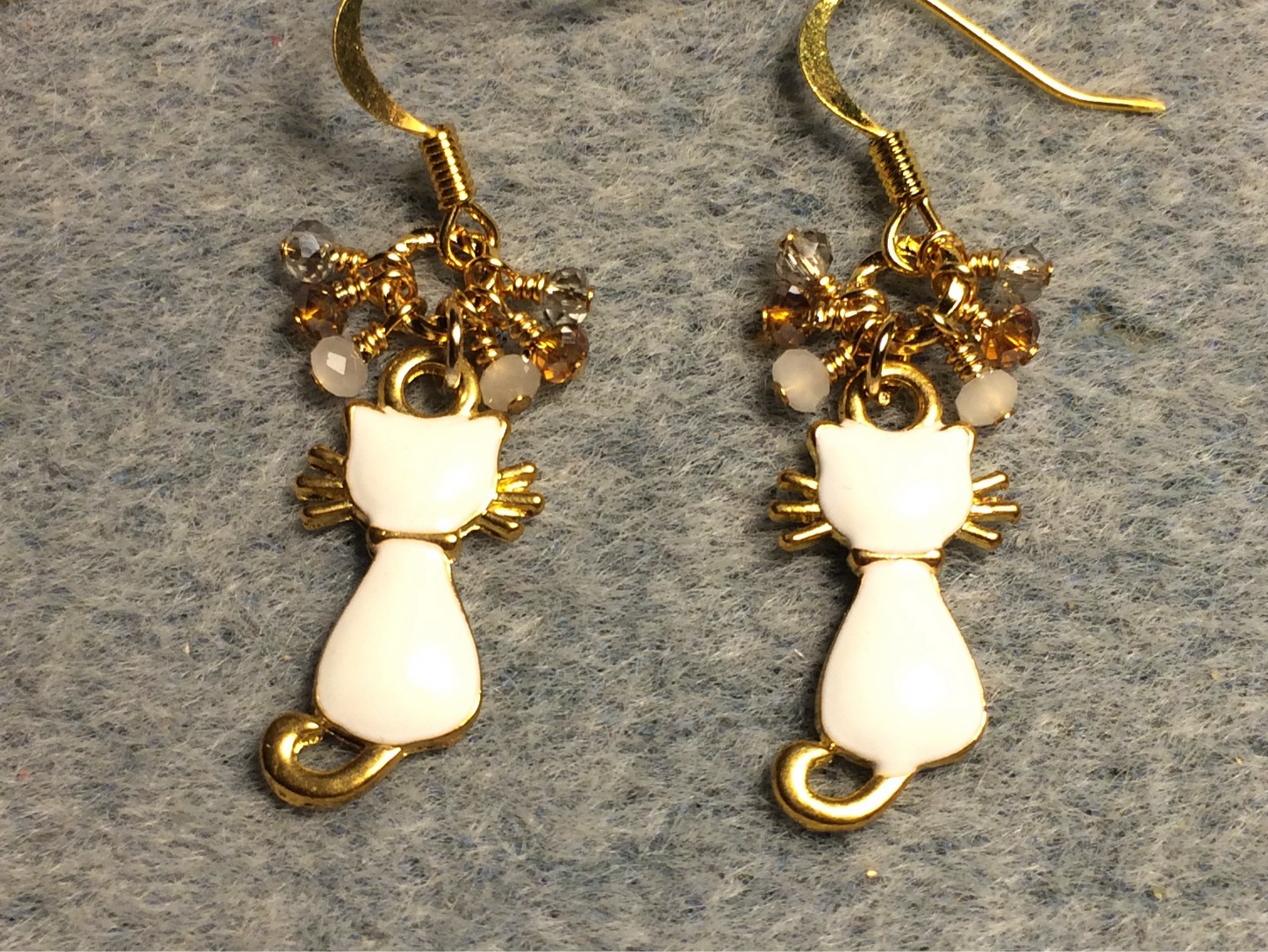 Small white and gold enamel cat charm earrings adorned with tiny dangling white, amber, and clear Chinese crystal beads.