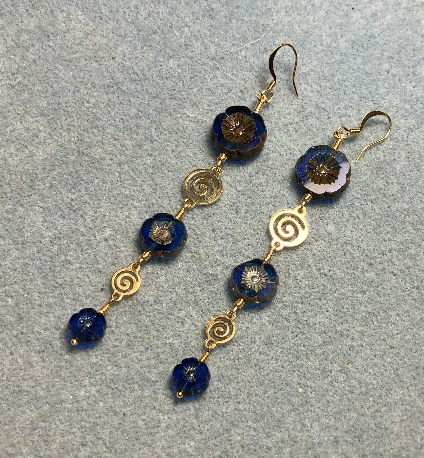 Extra long blue flower bead earrings made with three sizes of cobalt blue Czech glass pansy beads joined by gold swirly connectors.