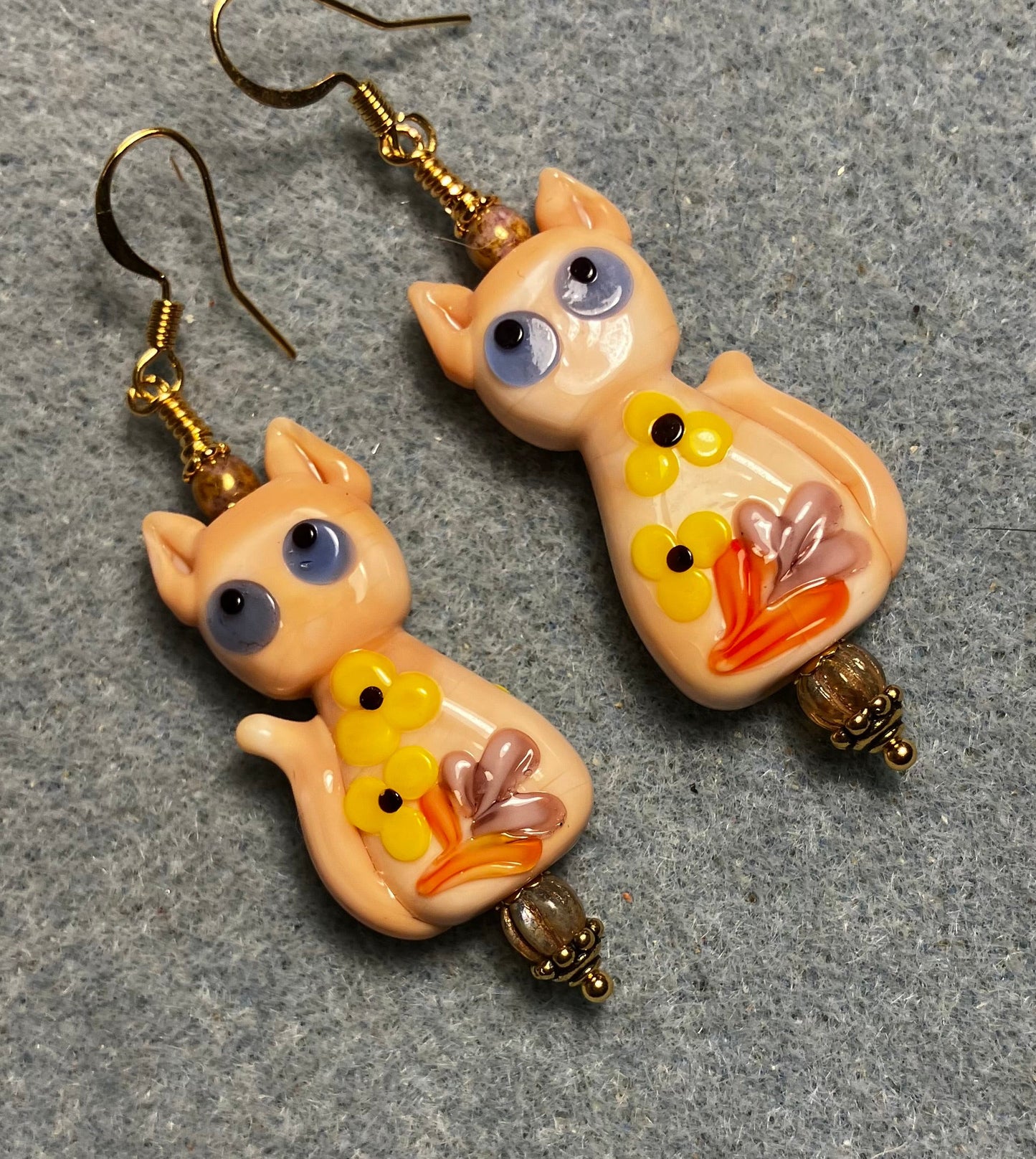 Large beige, orange, and yellow lamp work cat bead earrings adorned with beige Czech glass beads.