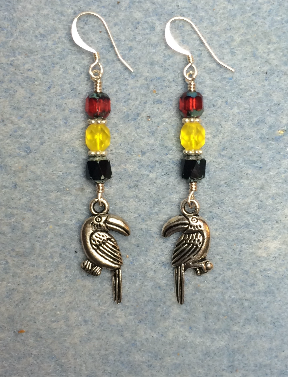 Silver toucan charm earrings adorned with black, yellow, and red Czech glass beads