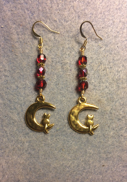 Gold cat sitting on a quarter moon charm earrings adorned with red Czech glass beads