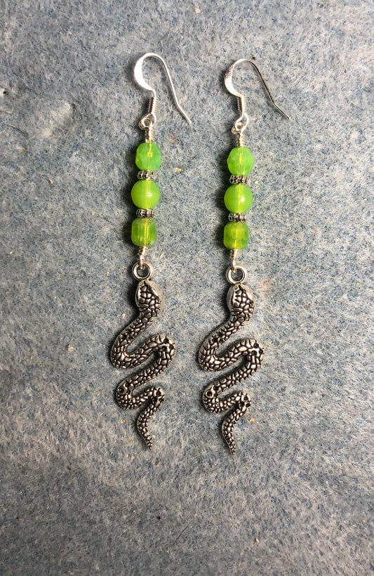 Long silver snake charm earrings adorned with lime green Czech glass beads.
