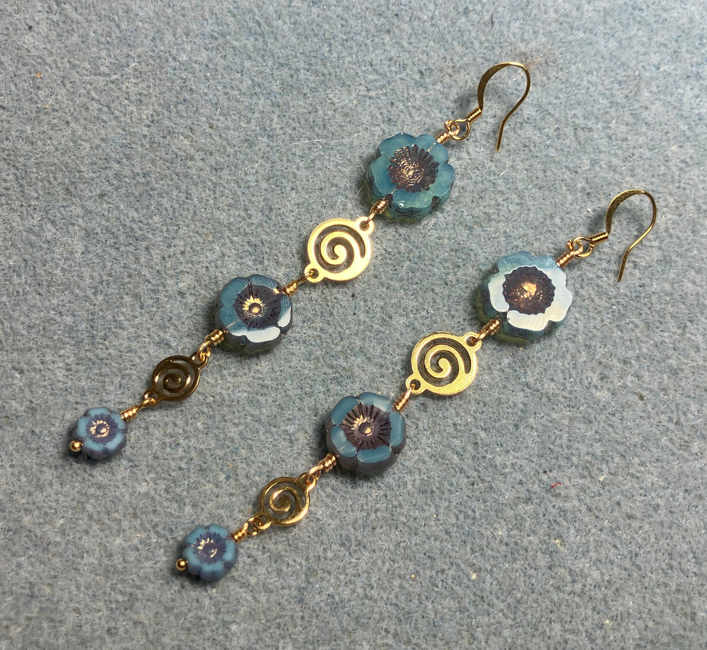 Extra long blue and copper flower bead earrings made with three sizes of blue and copper Czech glass pansy beads joined by gold swirly connectors.