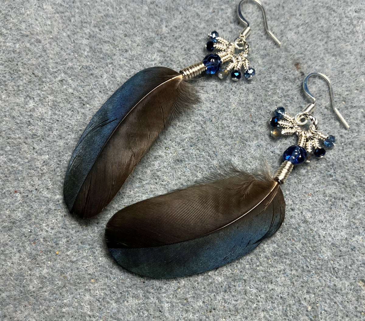 Small blue magpie feather earrings adorned with small blue Czech glass beads and tiny dangling blue Chinese crystal beads.