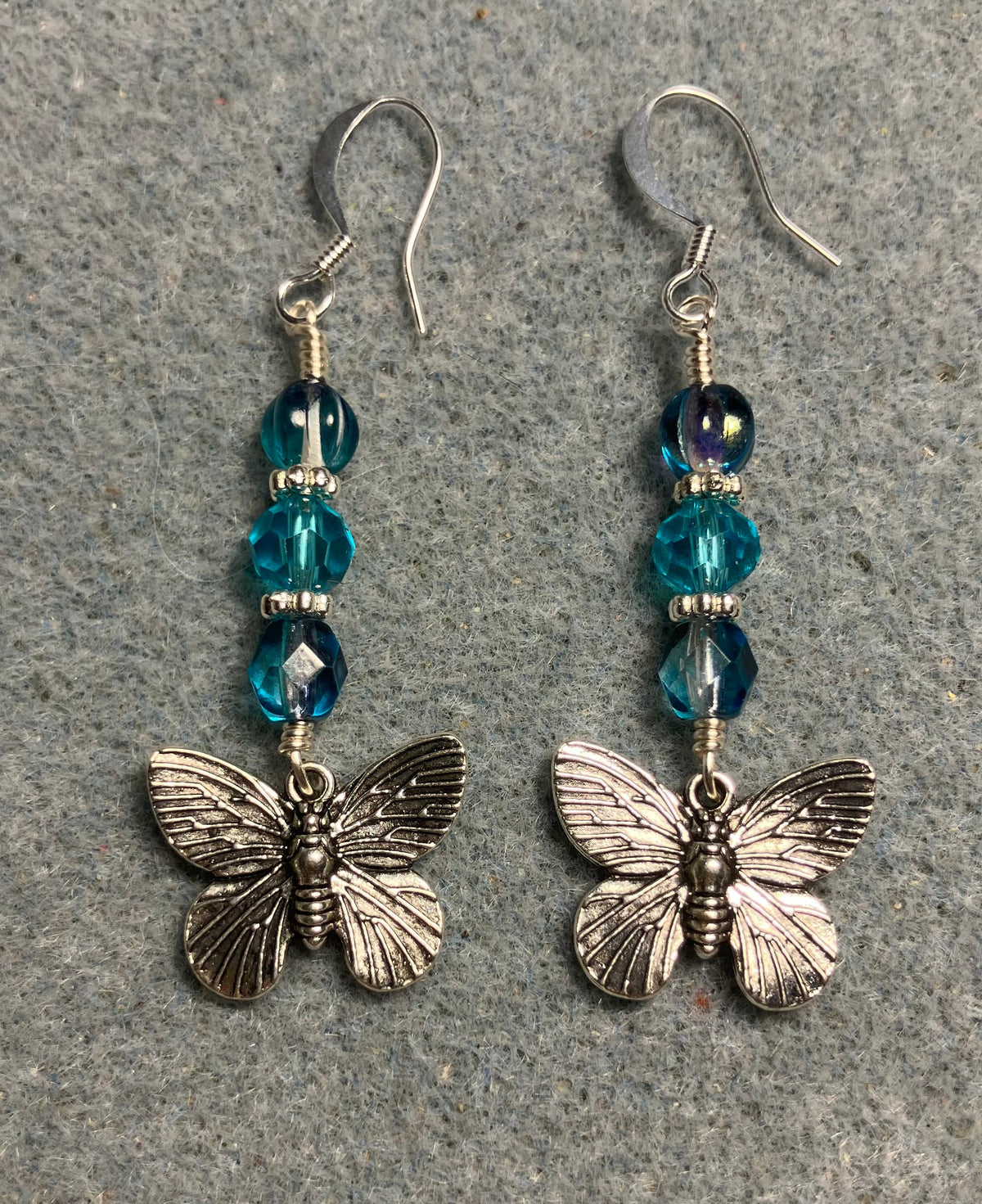 Silver butterfly charm earrings adorned with turquoise Czech glass beads.