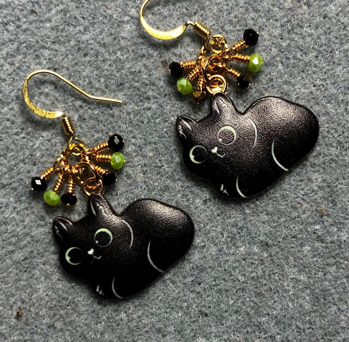 Black enamel cat charm earrings adorned with tiny dangling black, gold, and green Chinese crystal beads.