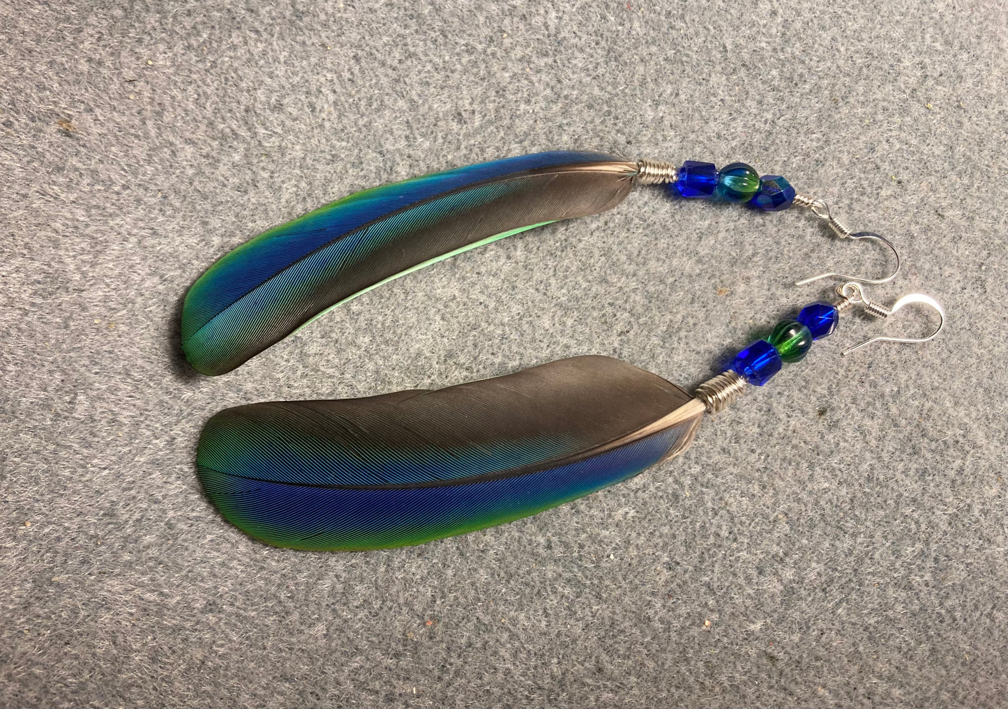 Very rare iridescent blue and green Pionus feather earrings adorned with blue and green Czech glass beads.