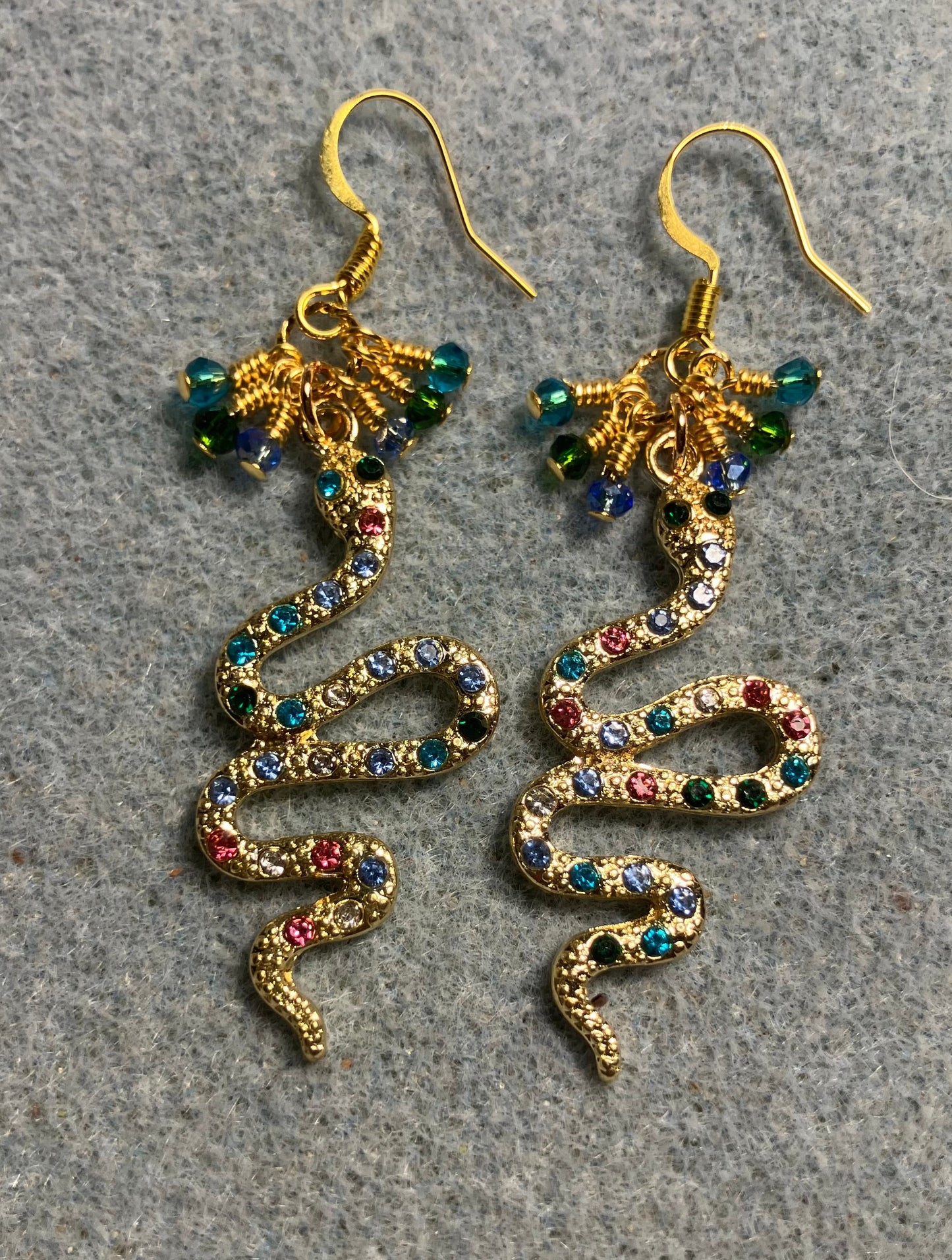 Gold and colored rhinestone coiled snake charm earrings adorned with tiny dangling turquoise, light blue, and dark green Chinese crystal beads.