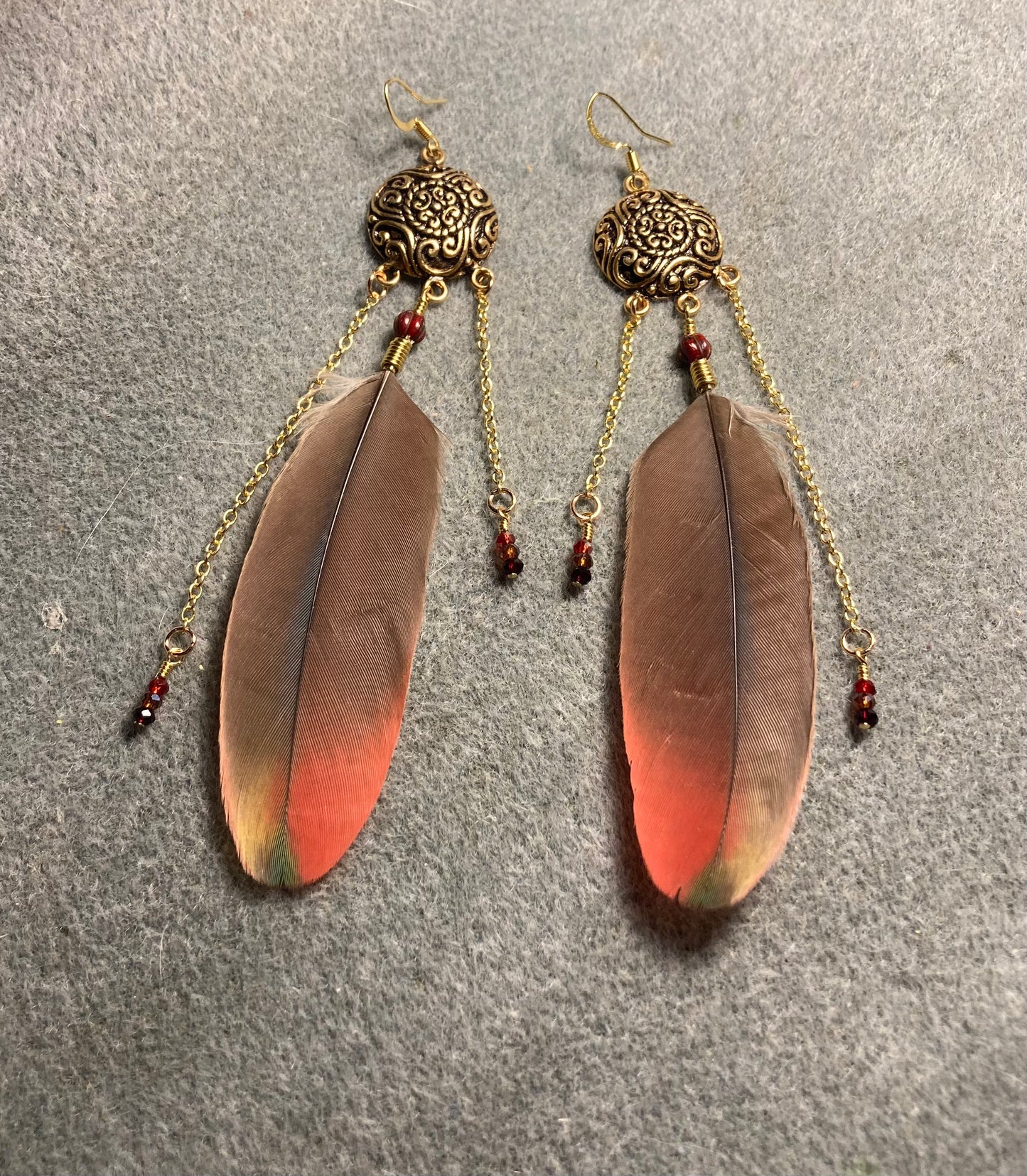 Scarlet macaw feather earrings attached to gold chandelier findings, gold chain, and tiny brown, dark red, and red Chinese crystal beads.