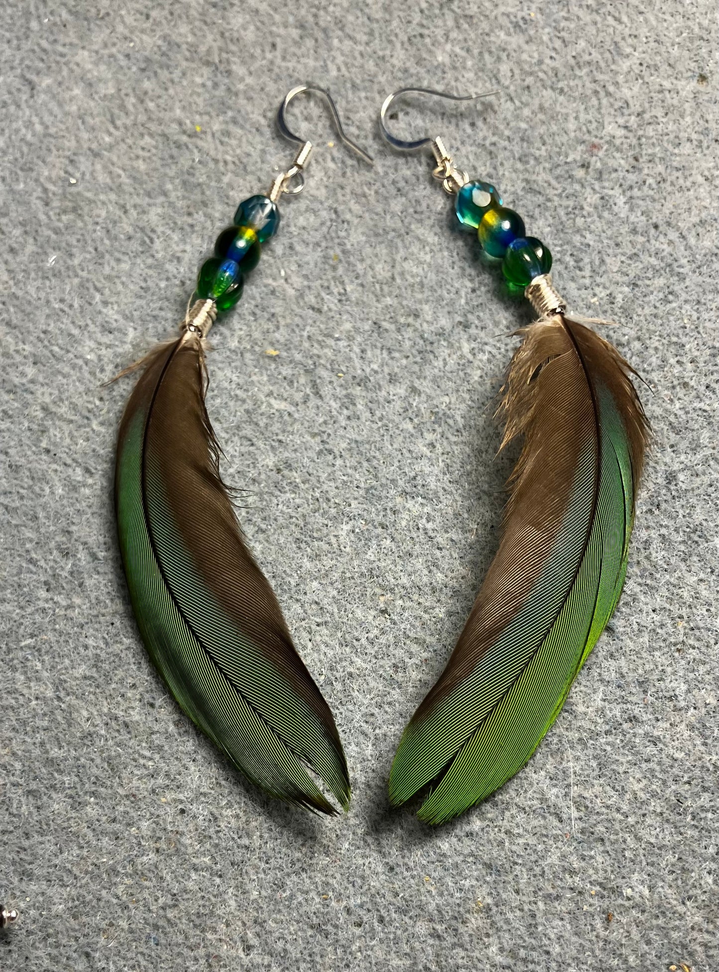 Bluish green mini macaw feather earrings adorned with green and teal Czech glass beads.