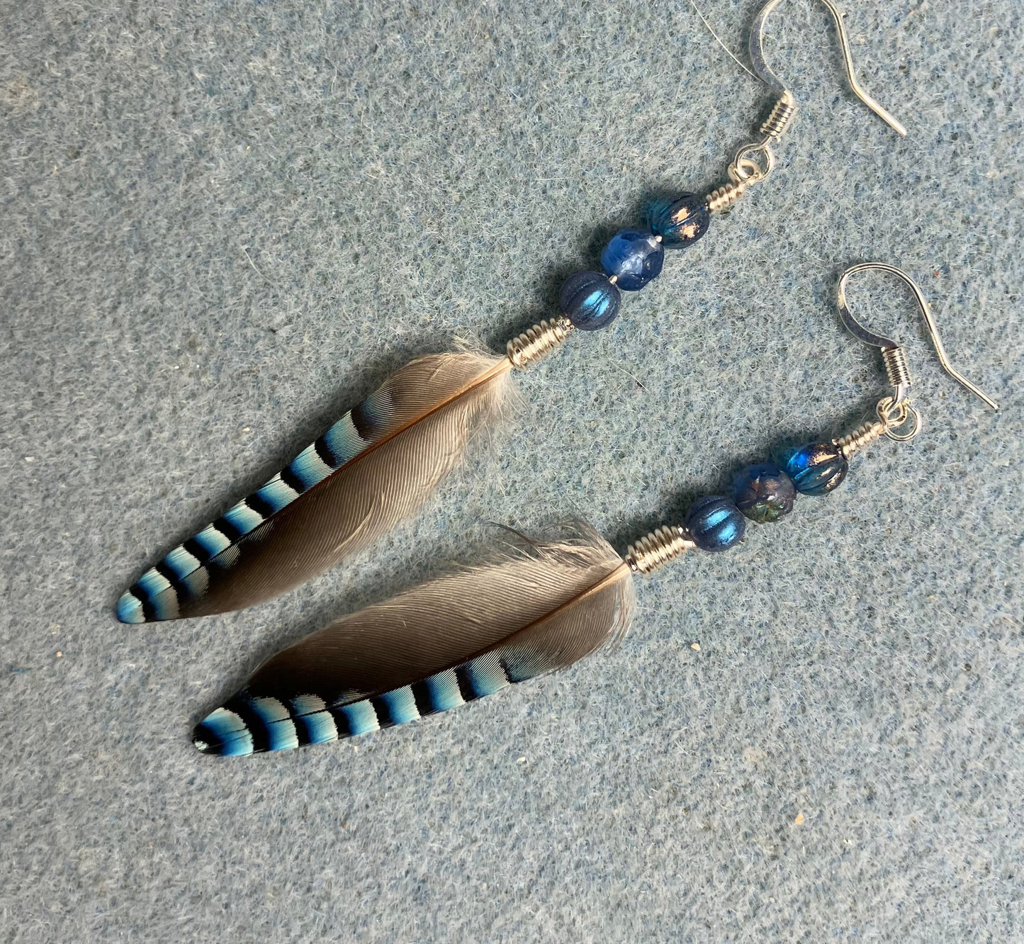 Small striped blue jay feather earrings adorned with small blue Czech glass beads.