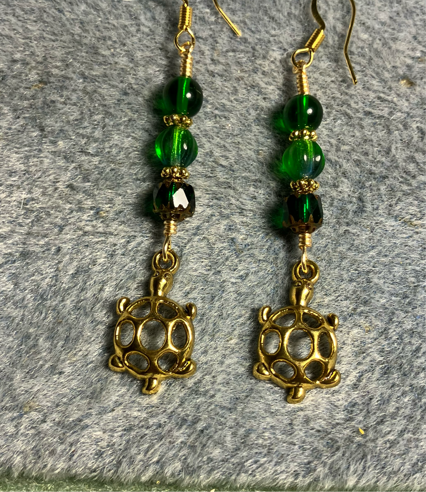 Gold turtle charm earrings adorned with emerald green Czech glass beads.