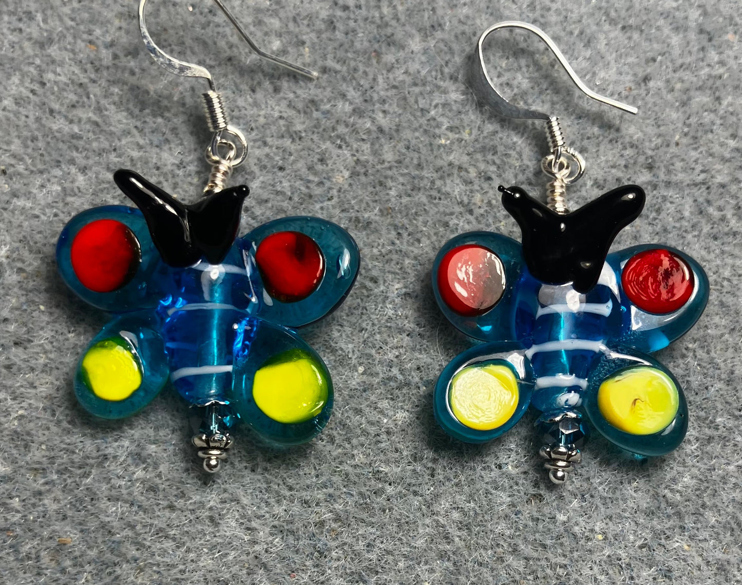 Turquoise, red, yellow, and black lamp work butterfly bead earrings adorned with turquoise Czech glass beads.