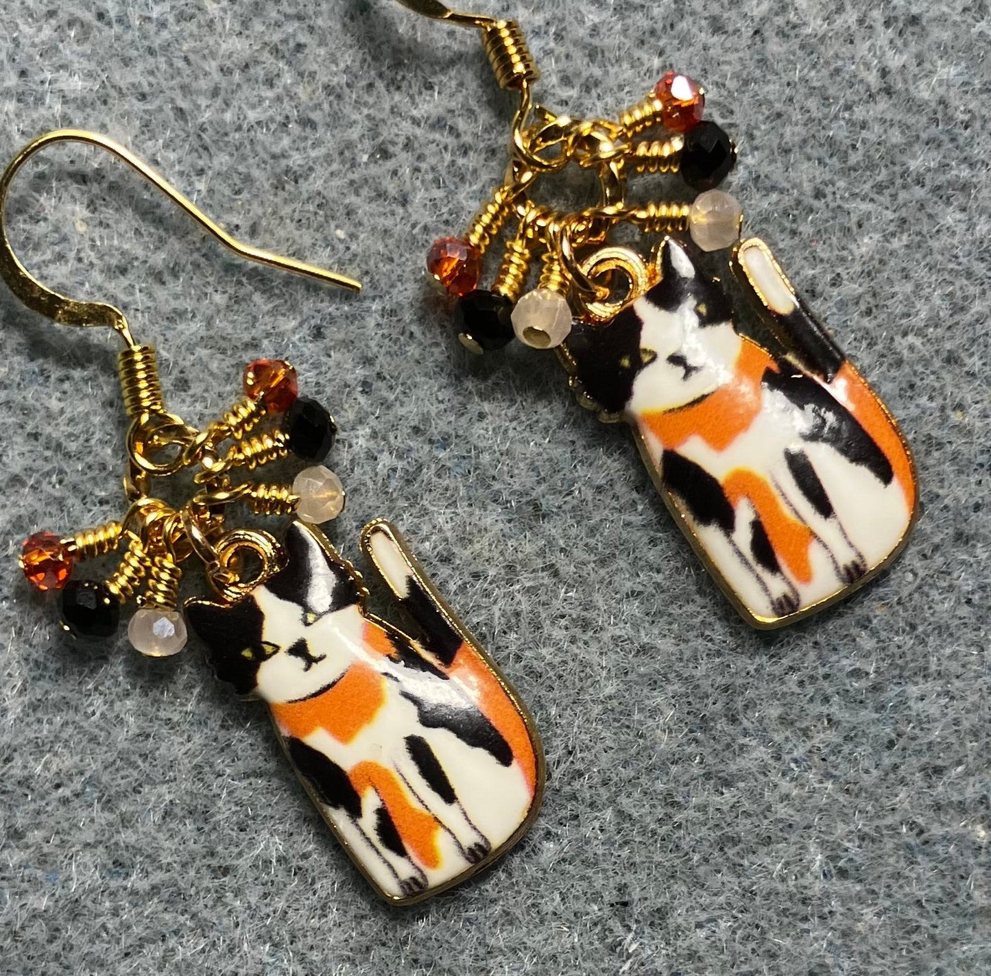 Black, orange, and white enamel calico cat charm earrings adorned with tiny dangling black, orange, and white  Chinese crystal beads.