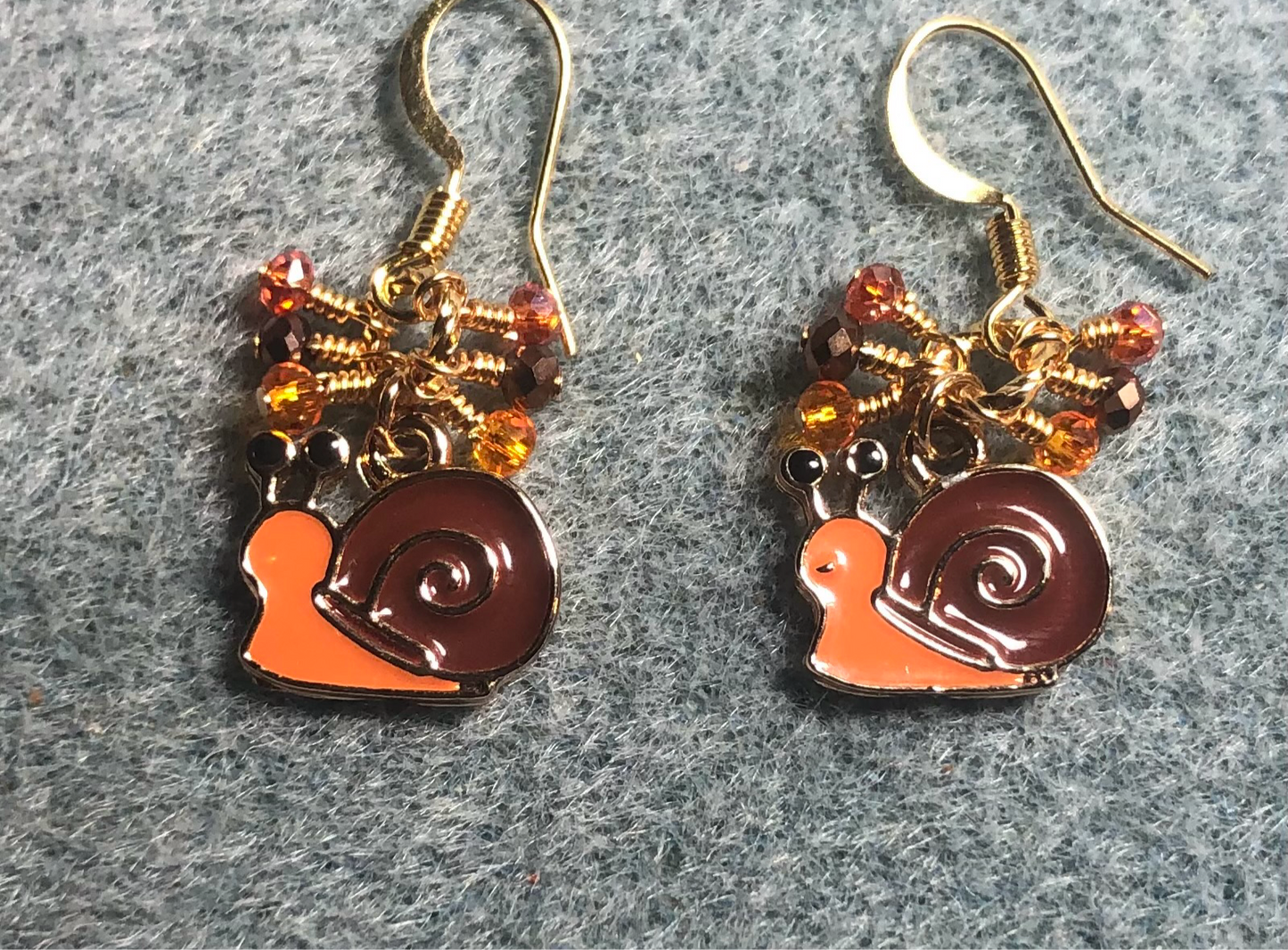 Small orange and brown enamel snail charm earrings adorned with tiny dangling orange and brown Chinese crystal beads.