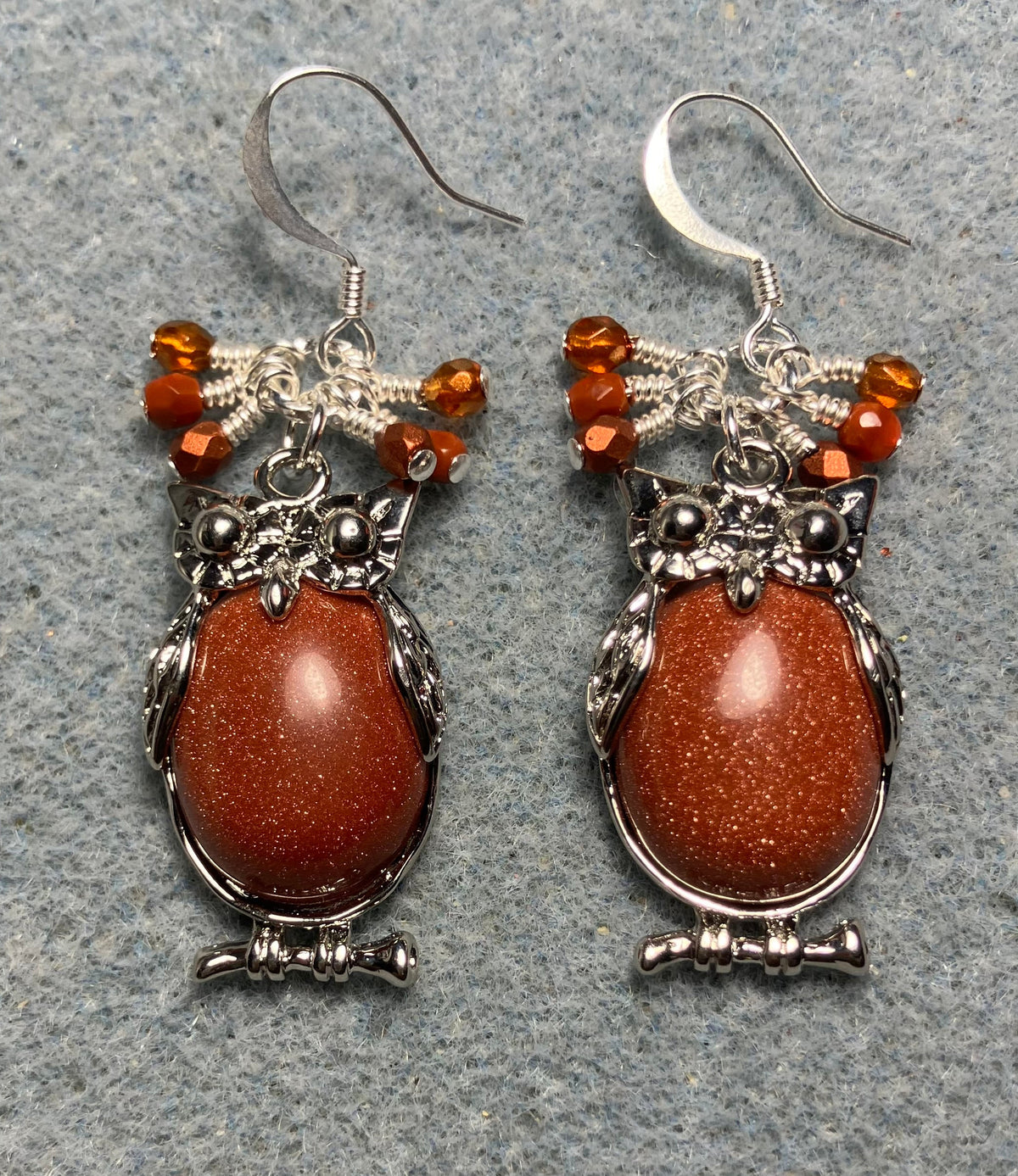 Large silver and orange goldstone gemstone owl charm earrings adorned with small dangling orange Czech glass beads.