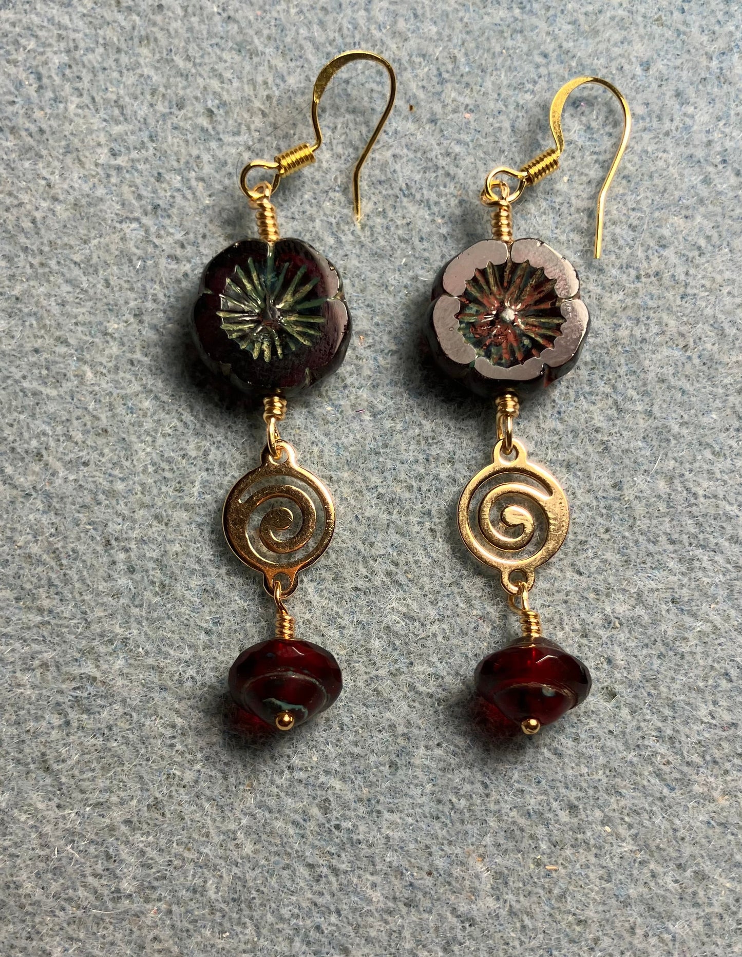 Dark red Czech glass pansy bead earrings adorned with gold swirly connectors and dark red Czech glass Saturn beads.