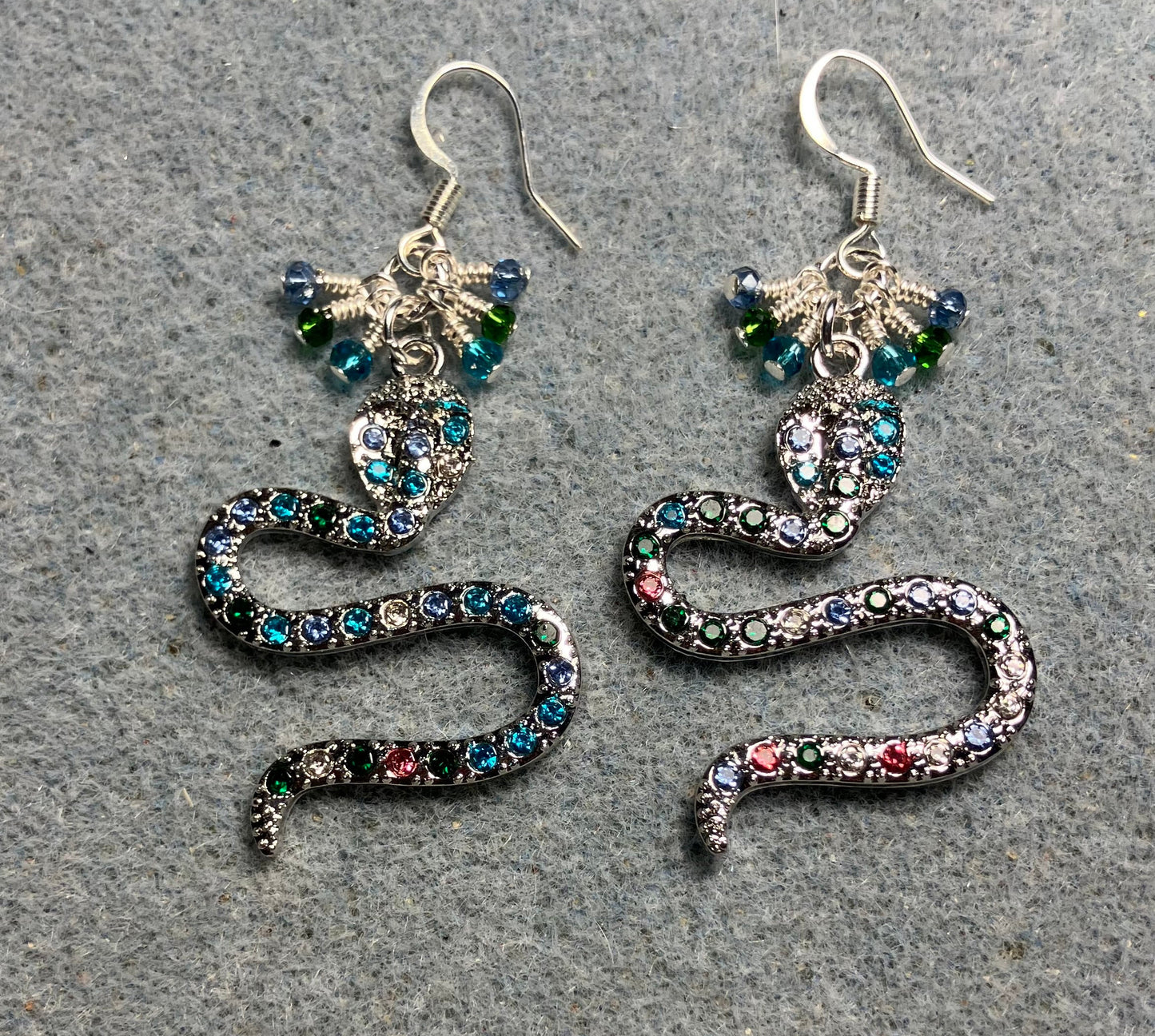Silver and colored rhinestone coiled snake charm earrings adorned with tiny dangling turquoise, dark green, and light blue Chinese crystal beads.
