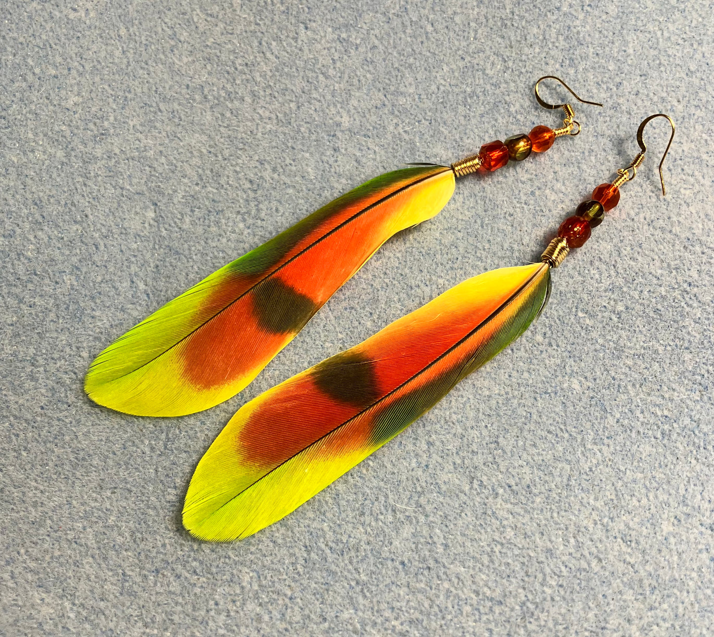 Orange winged Amazon tail feather earrings adorned with orange and green Czech glass beads.